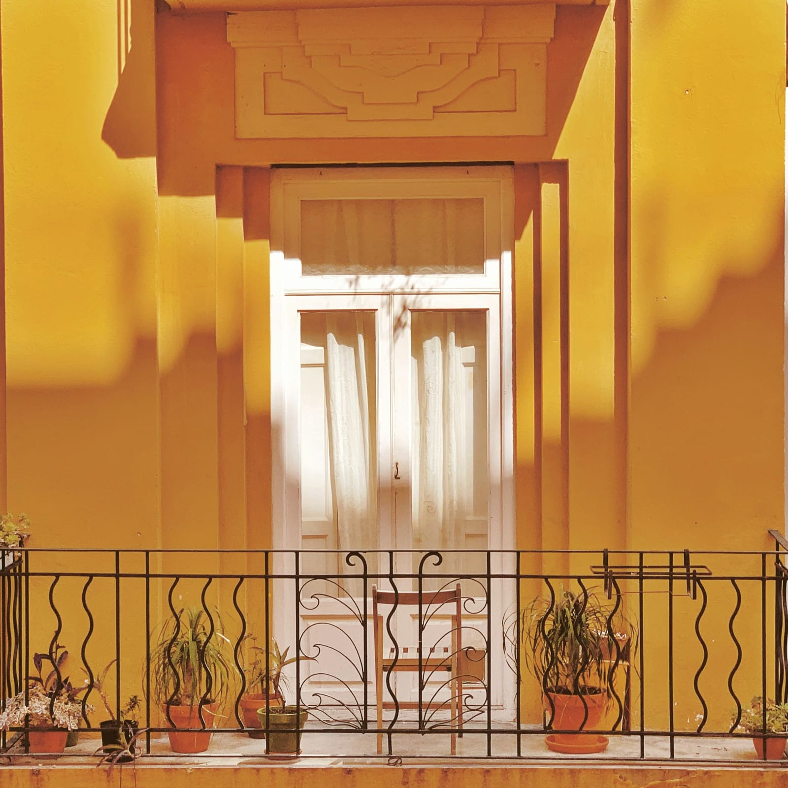 A yellow Spanish balcony with wrought iron railing and potted plants