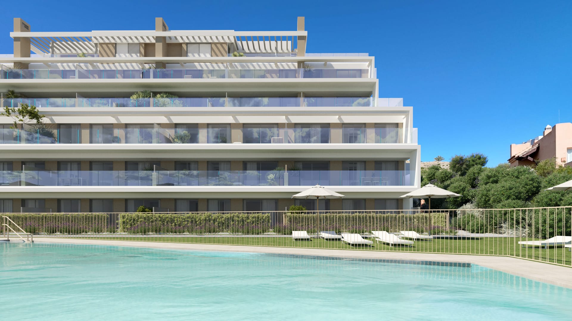 The pool, with sunloungers on the lawn and the terraces of the buildings rising behind it. Aire, Cancelada, Estepona.