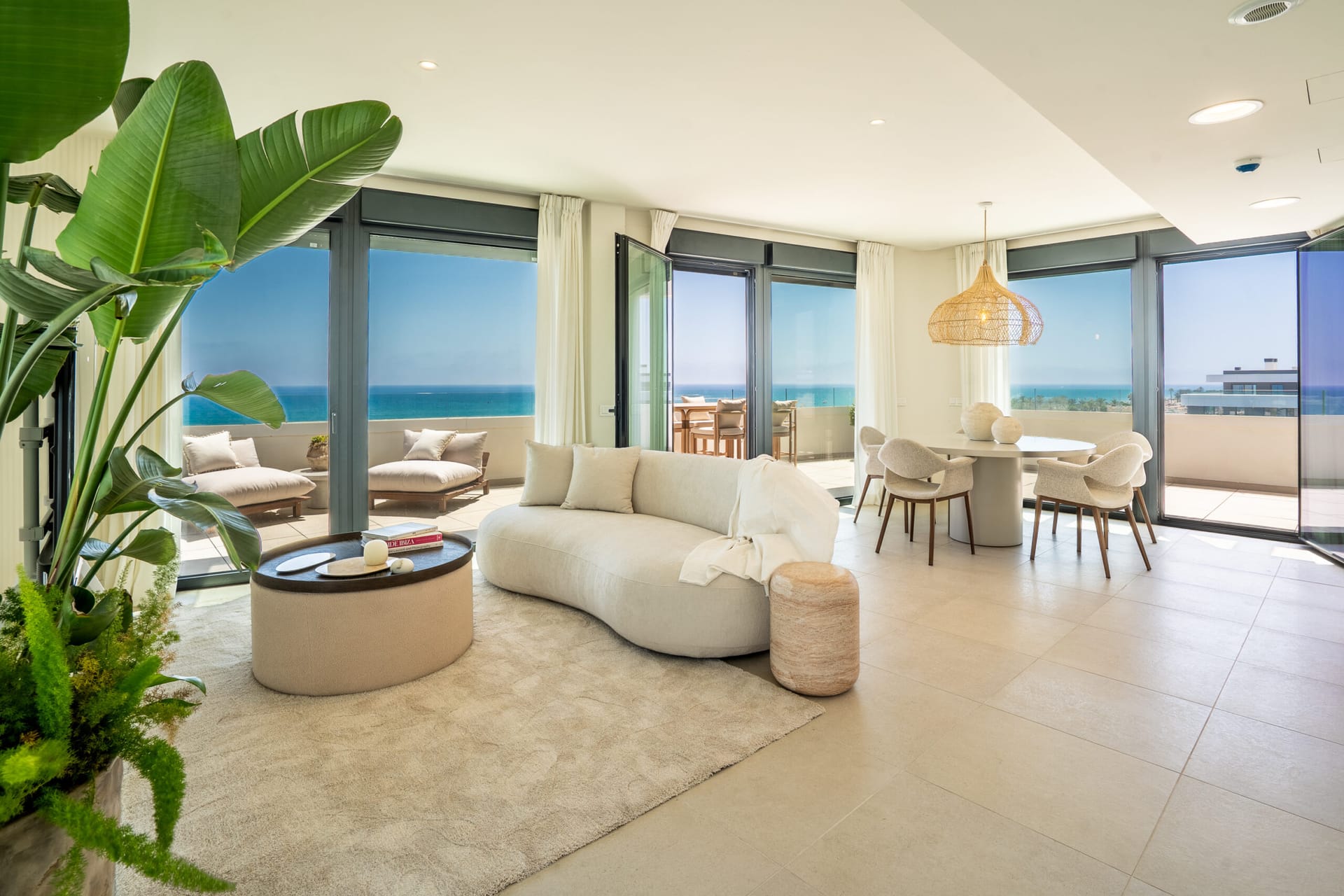 A living and dining room glazed on two sides, opening onto the terrace with the sea beyond. Alborán Bora, Los Álamos, Torremolinos.