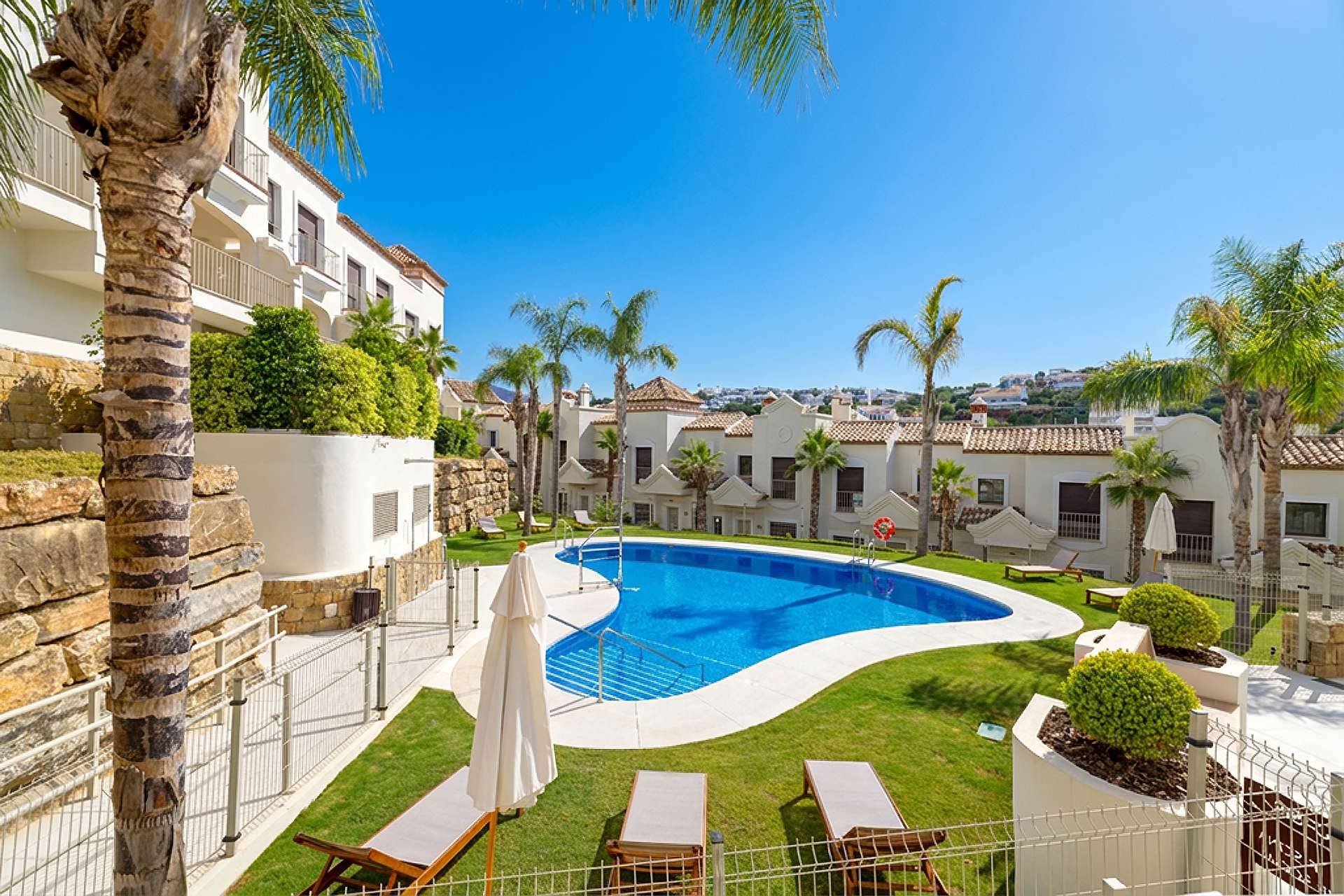 The outdoor pool in its lawn, with palm trees and a row of the townhouses behind it. Altoasis, Azata Golf, Estepona.