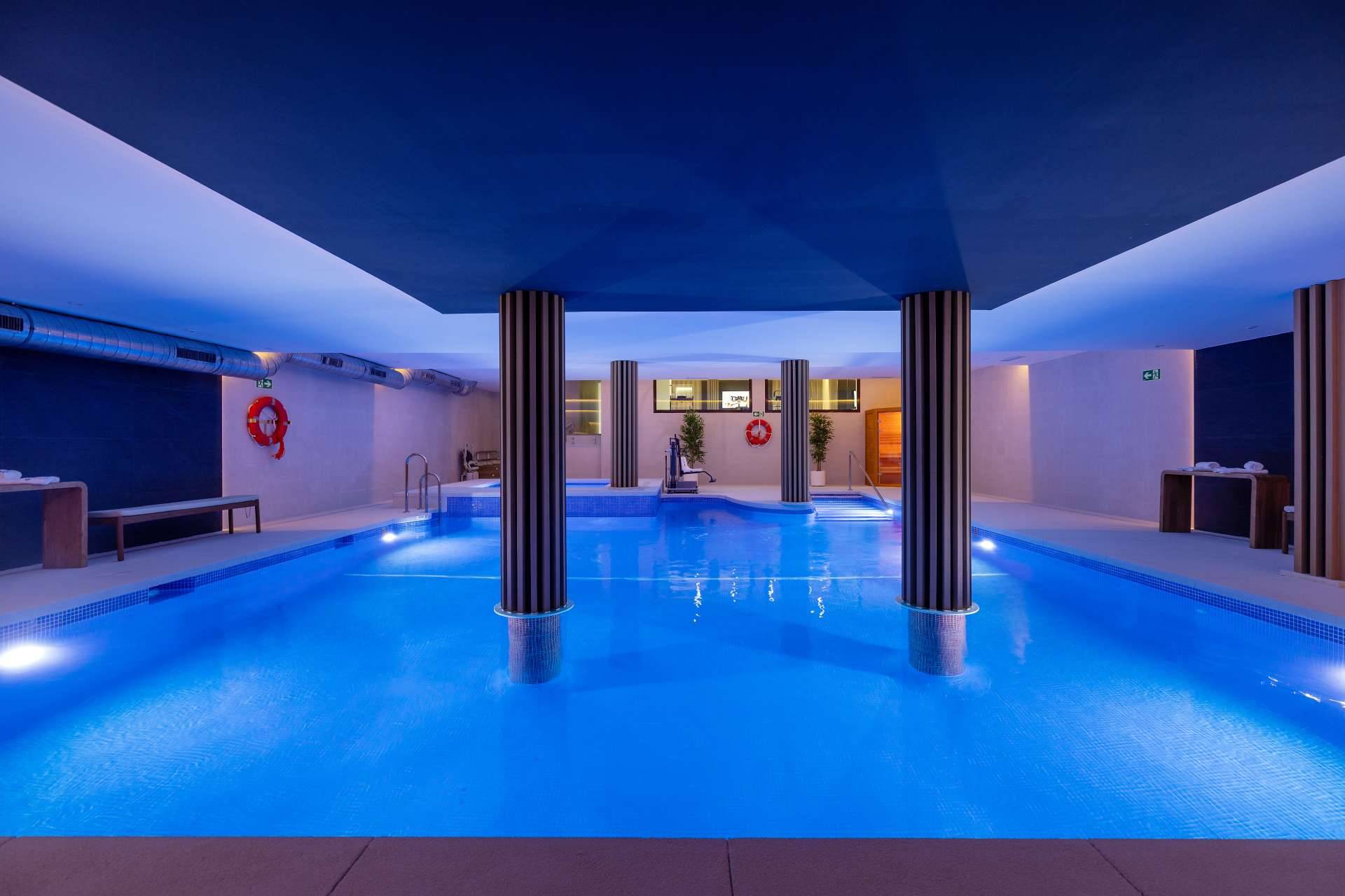 The heated indoor pool, lit blue, with two columns standing in the water. Altoasis, Azata Golf, Estepona.