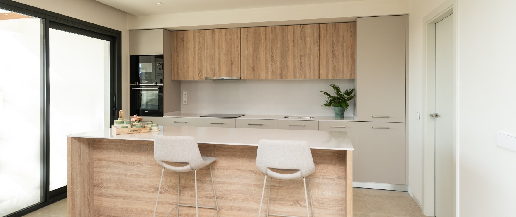 The kitchen, with oak and cream units, an oak-fronted island with two stools, and the oven and microwave set into a tall unit. Altura 160, Señorío de Cifuentes, Benahavís.
