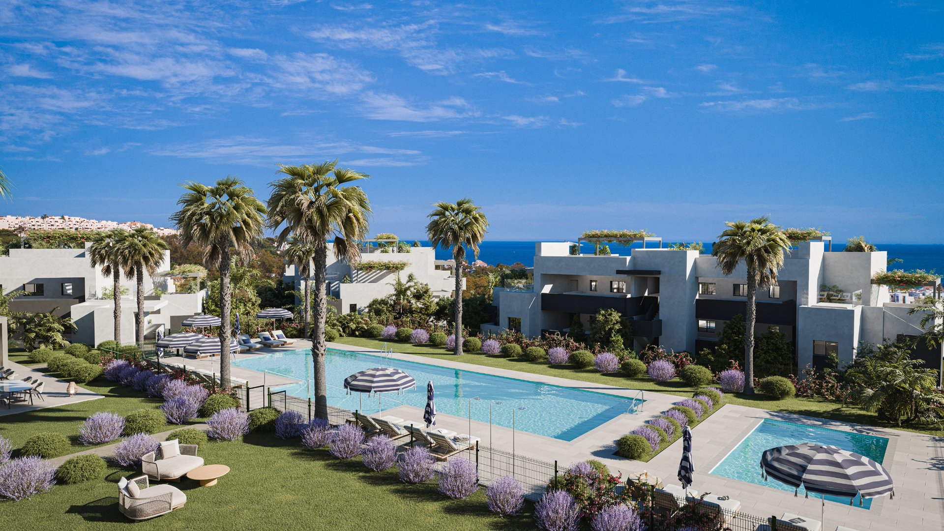The communal pool, with lawns and lavender around it, the buildings behind and the sea on the horizon. Alura Living, Casares Costa, Casares.
