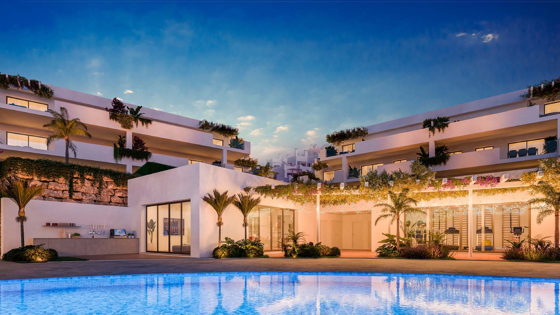 The buildings at dusk seen across the water, terraces lit from within and planting spilling over their edges. Amaranta Living, Casares Costa Golf, Casares.