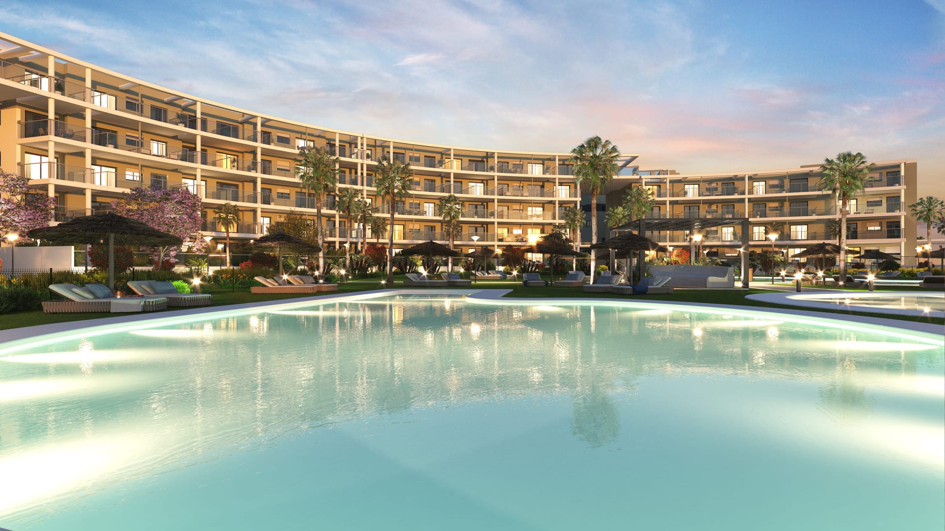 One of the communal pools at dusk, with loungers and palm trees in front of the curved apartment buildings. Amphora Beach Residence, La Chullera, Manilva.