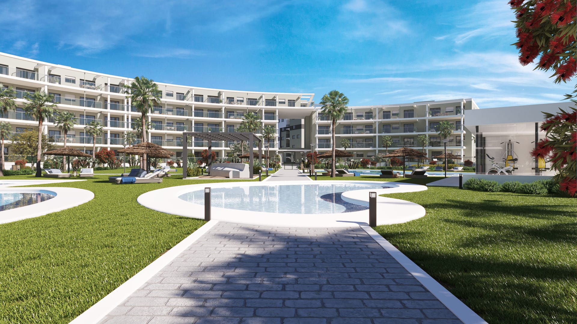 A paved path across the lawns to one of the pools, with the gym in a glass-fronted building on the right. Amphora Beach Residence, La Chullera, Manilva.