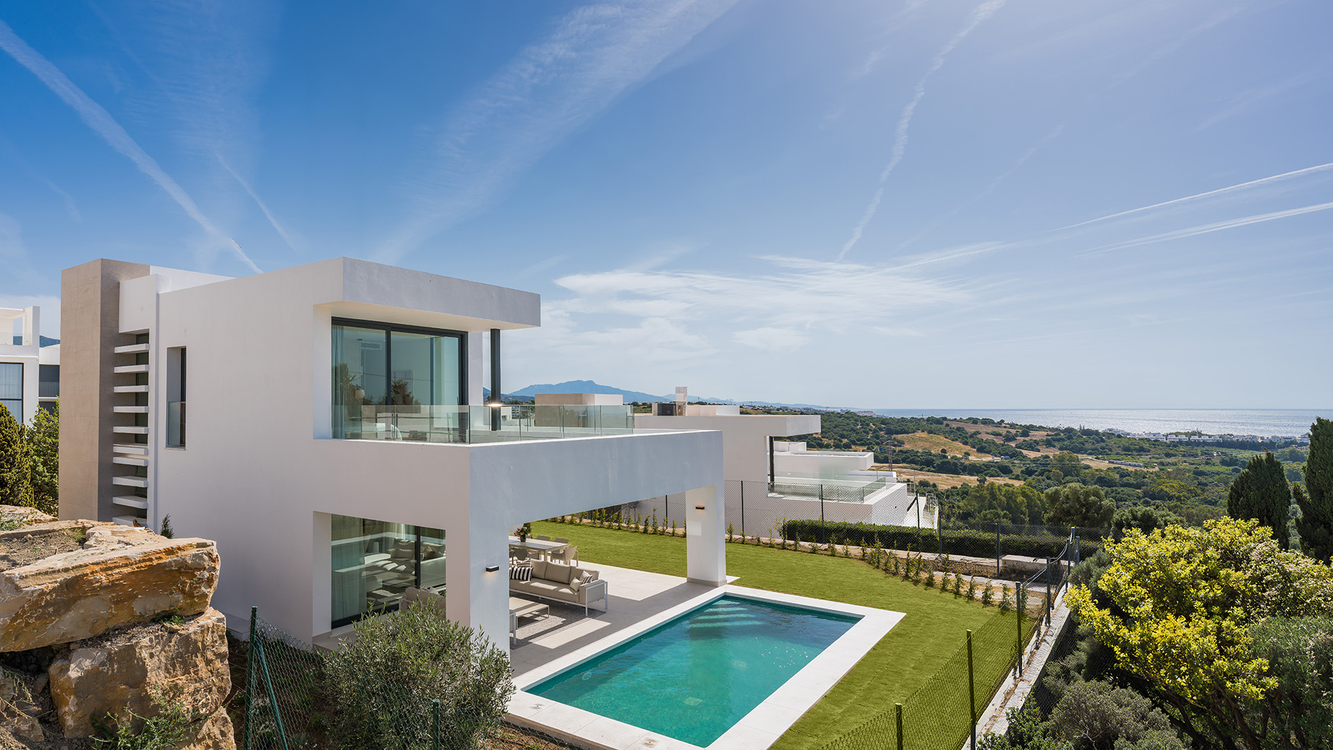 The show villa from the slope above it, with its pool and lawn below the terrace and the coast in the distance. Aurea Villas, Estepona Golf, Estepona.