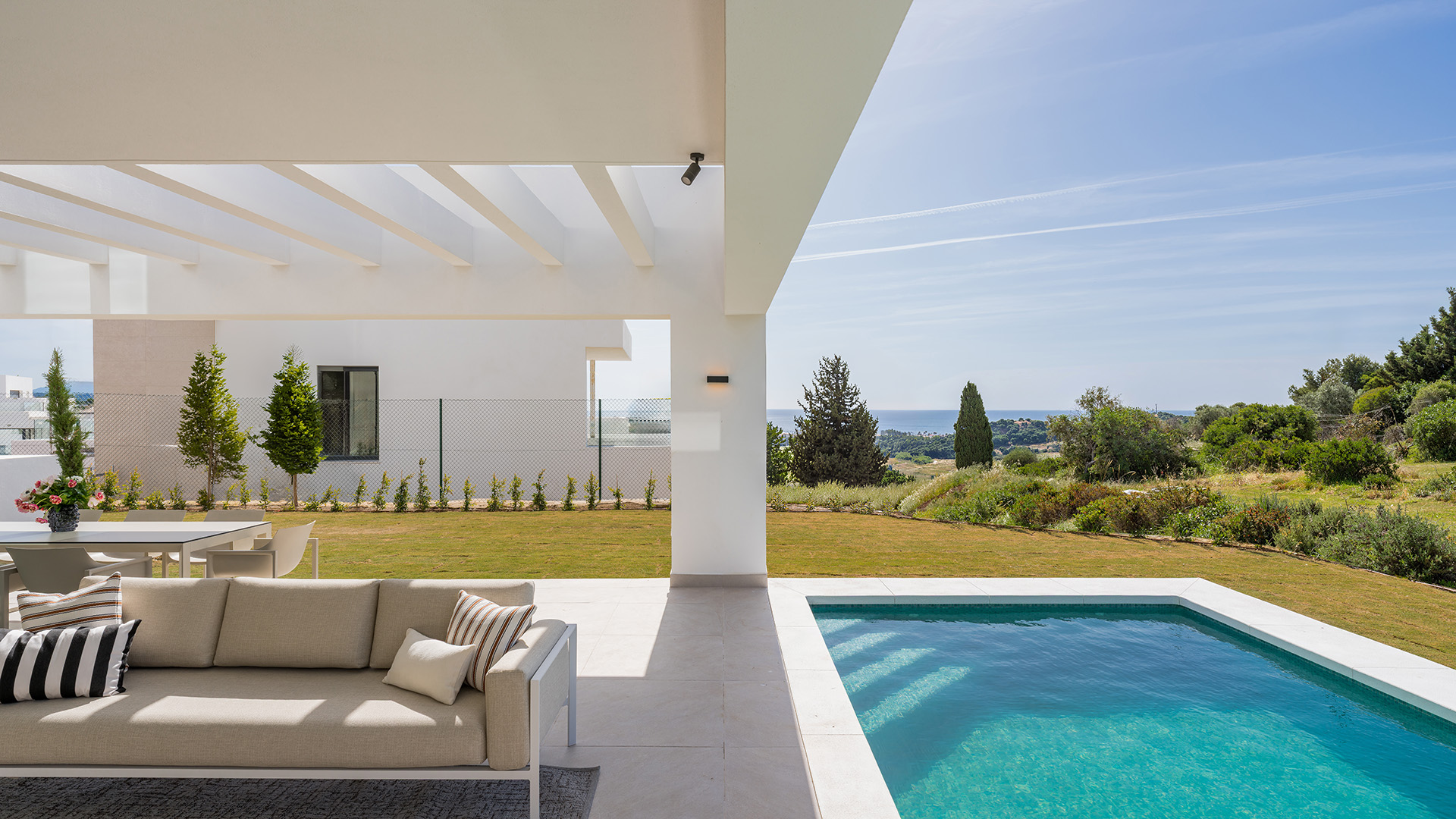 The covered terrace of the show villa, with the pool beside it and the sea on the horizon beyond the garden. Aurea Villas, Estepona Golf, Estepona.
