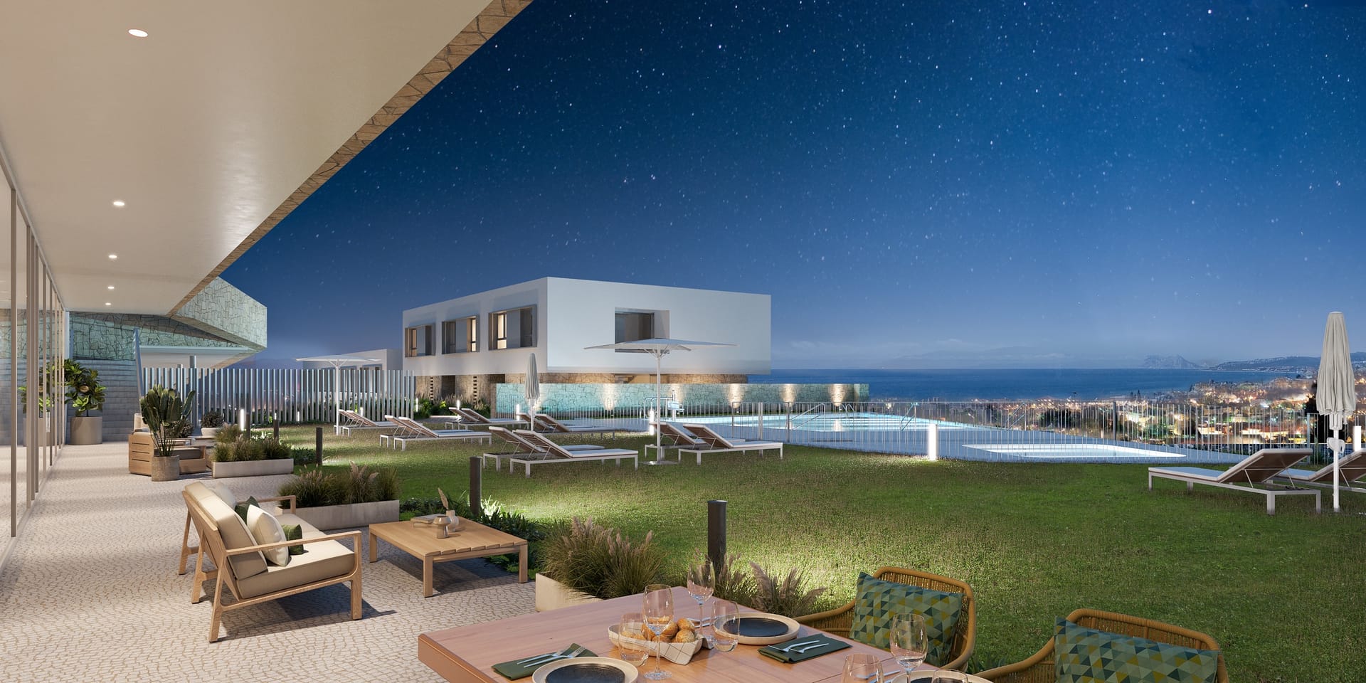 The garden and a pool at night, seen from a covered terrace with outdoor sofas, with the sea on the horizon. Azure Estepona, La Gaspara, Estepona.