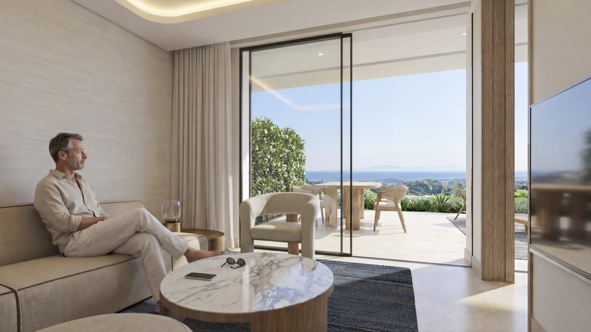 The living room of one of the apartments, furnished, with glass doors to the terrace and the sea in the distance. Azurean Marbella, La Reserva de Alcuzcuz, Benahavís.