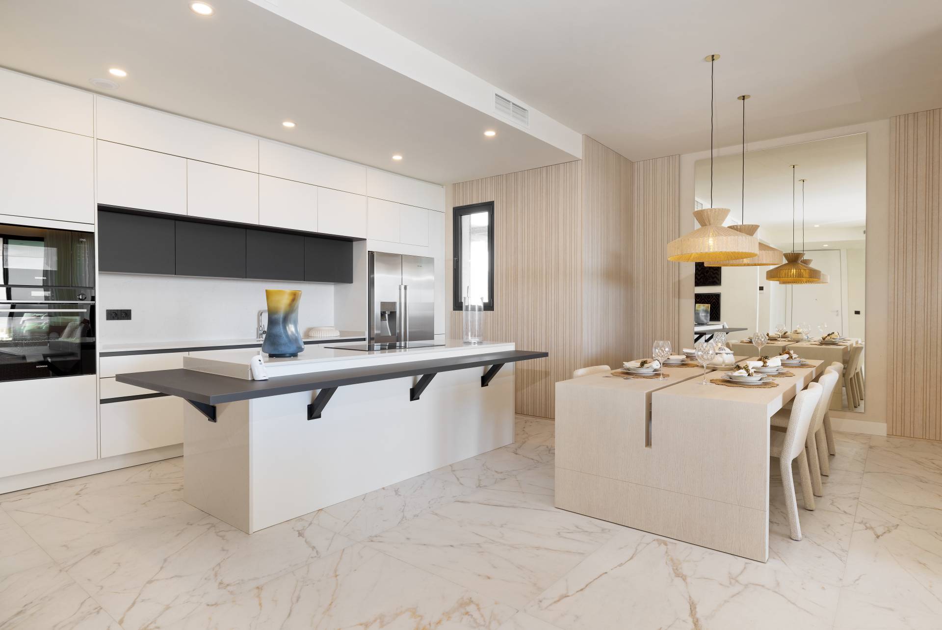 A kitchen with white units, an island with a dark grey breakfast bar, and the dining table beside it. Balcón del Mediterráneo, New Golden Mile, Estepona.