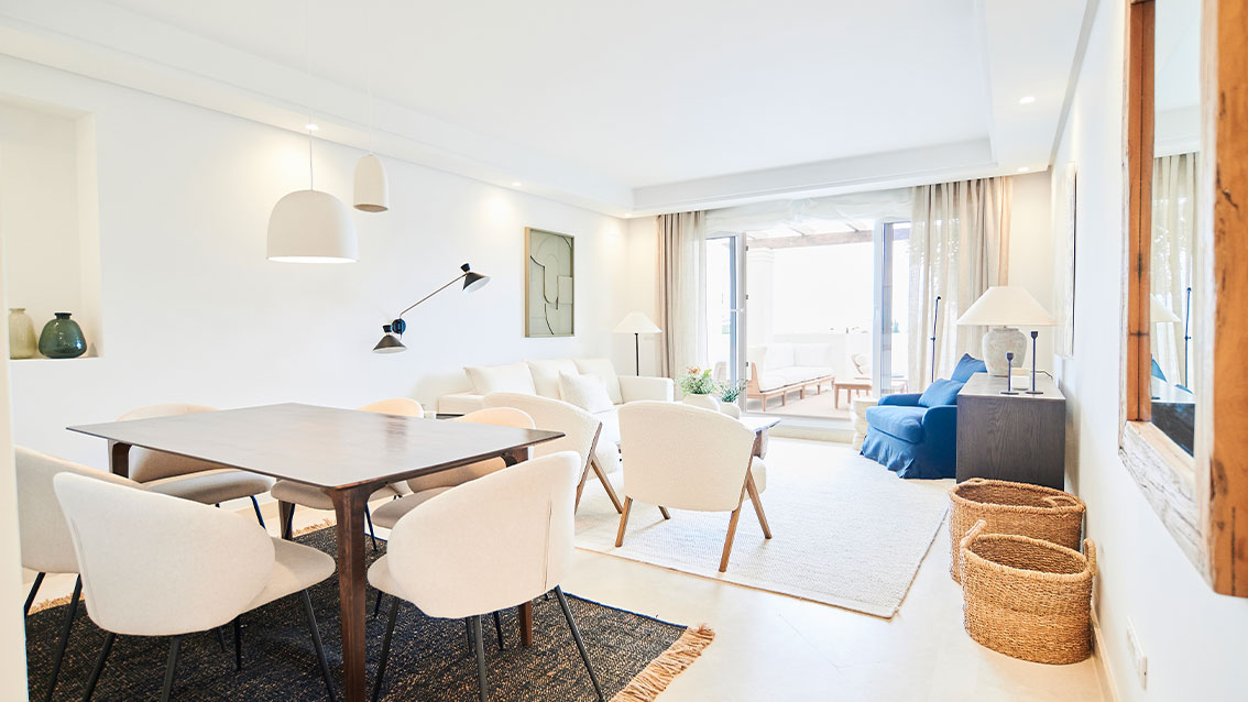 A living and dining room, with cream marble floors and glass doors open to the terrace. Be Aloha, Nueva Andalucía, Marbella.