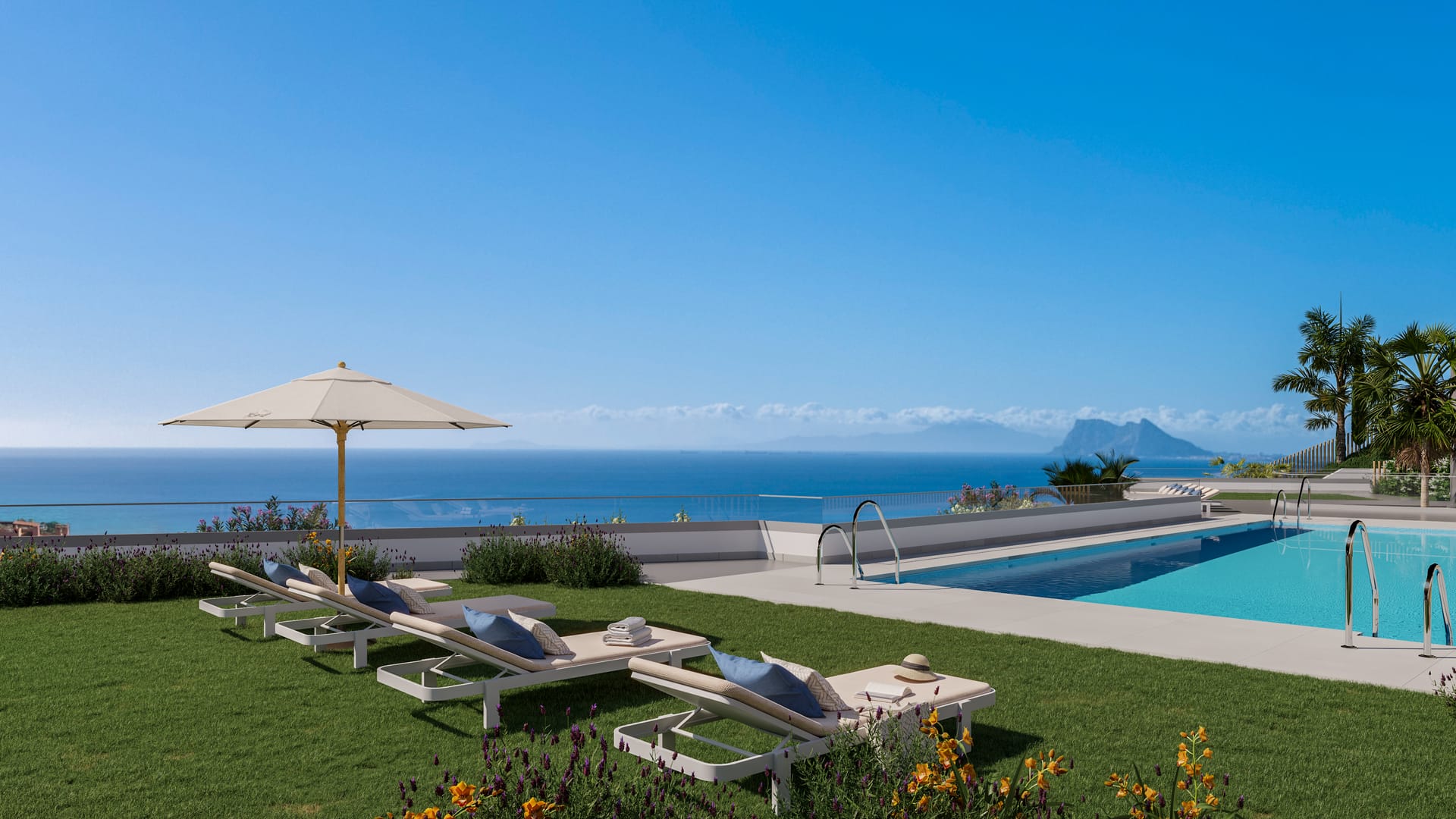 The community pool, with sun loungers and a parasol on the lawn beside it and the sea and the Rock of Gibraltar on the horizon. Blue Marine, La Chullera, Manilva.