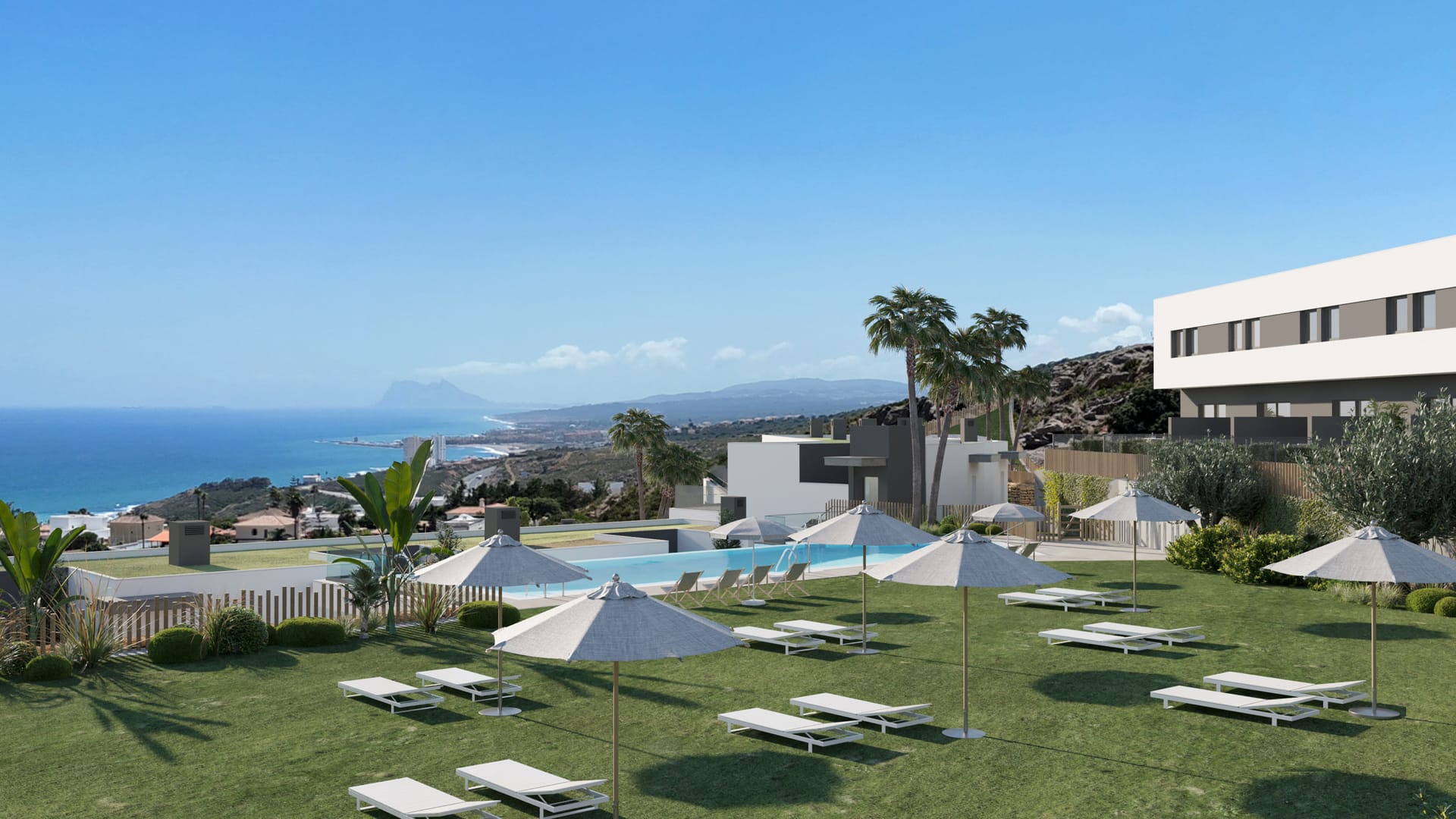 The community pool and its lawn set with loungers and parasols, with the coast and the Rock of Gibraltar beyond. Blue Wave, La Chullera, Manilva.