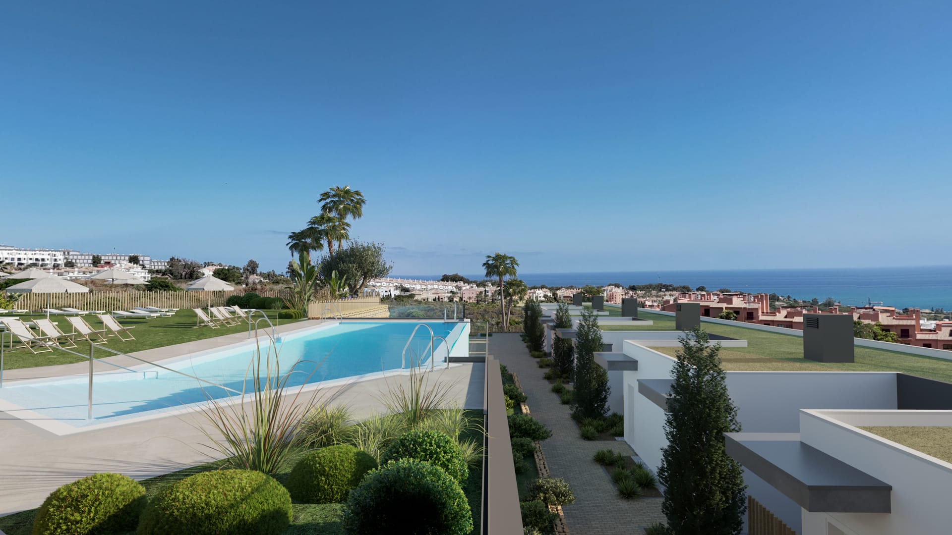 The community pool beside a paved path between the homes, with the sea in the distance. Blue Wave, La Chullera, Manilva.