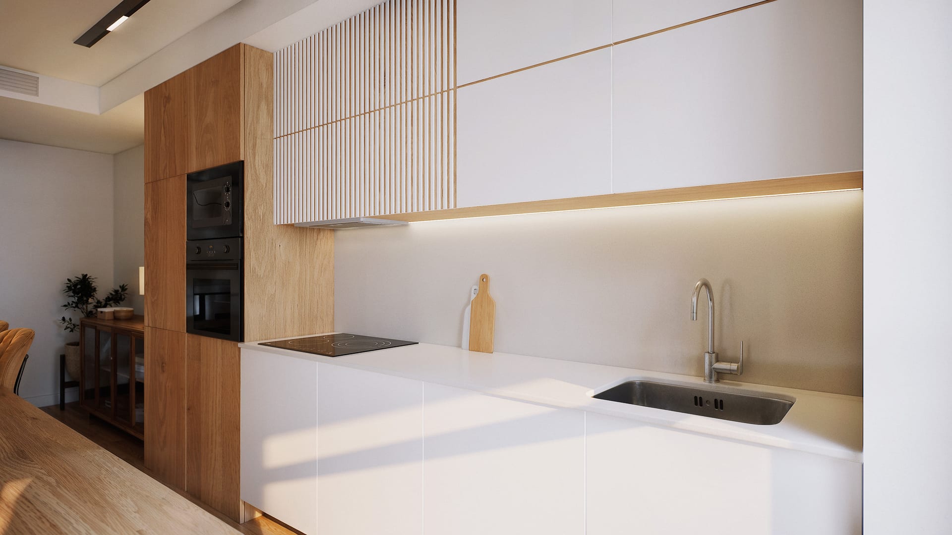 A kitchen in white and timber, with the oven and microwave built into a timber column and a strip of light beneath the wall cupboards. Bulevar 360, Cortijo Merino, Málaga.