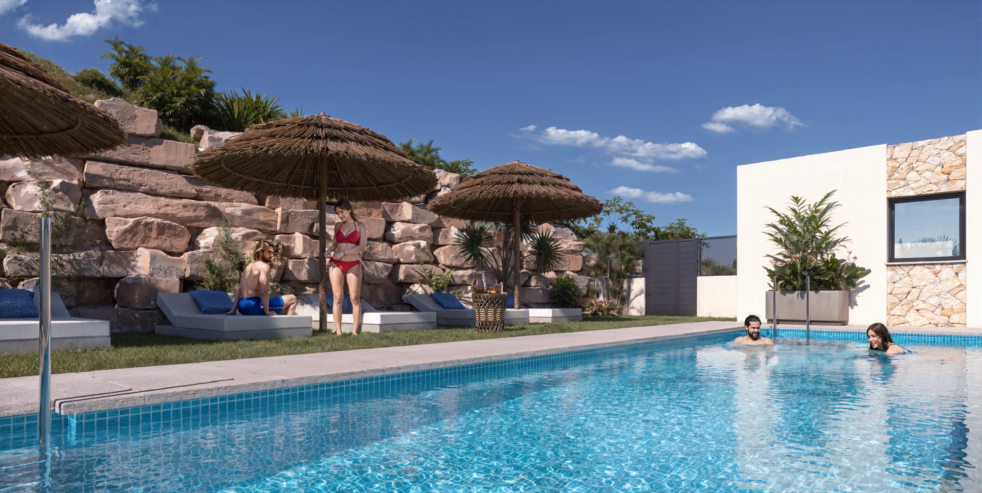 The communal pool behind the houses, with loungers on the lawn under a rock retaining wall. Cala Golf, Entrerríos, Mijas.