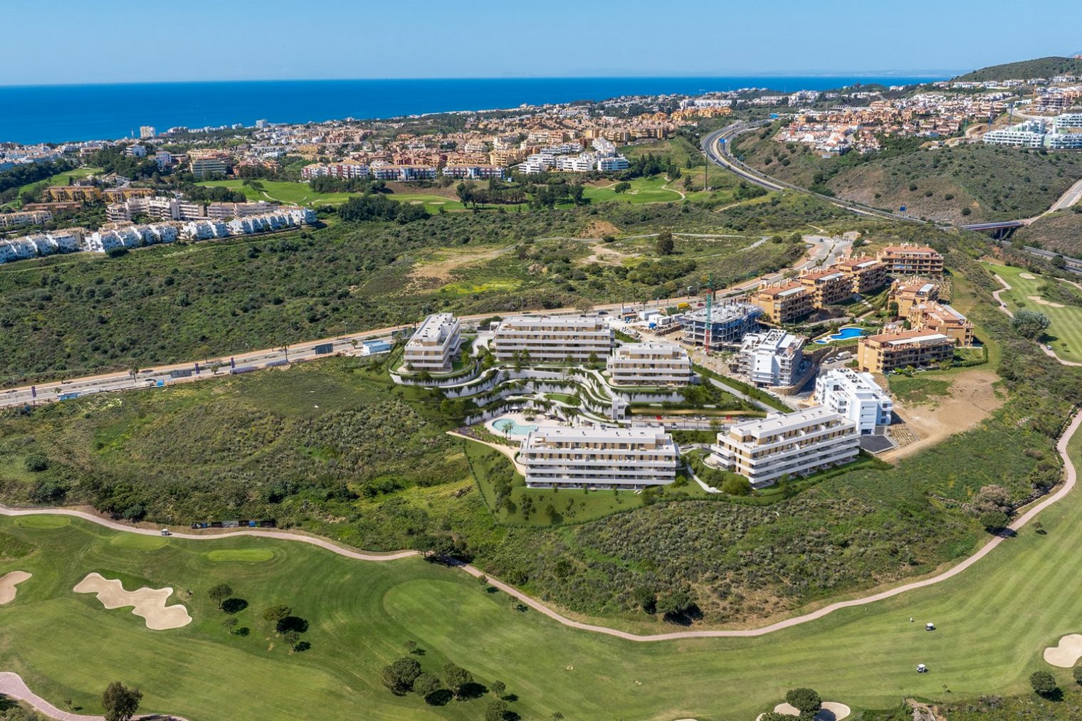 The scheme from the air, its buildings stepped down the hillside above the fairways, with La Cala de Mijas and the sea beyond. Cala Swing, La Cala de Mijas, Mijas.
