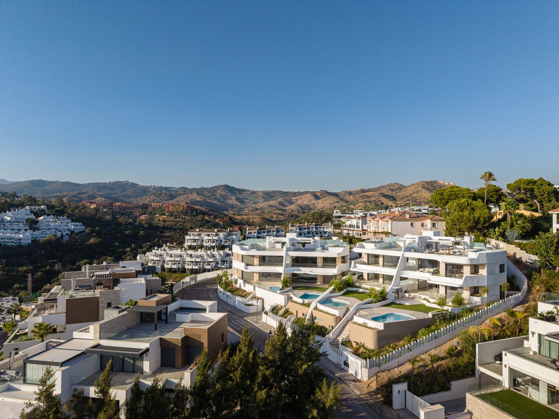 An aerial view of the development on its hillside, with gardens and private pools in front of the homes and hills behind. Golden Eight, Cabopino, Marbella.