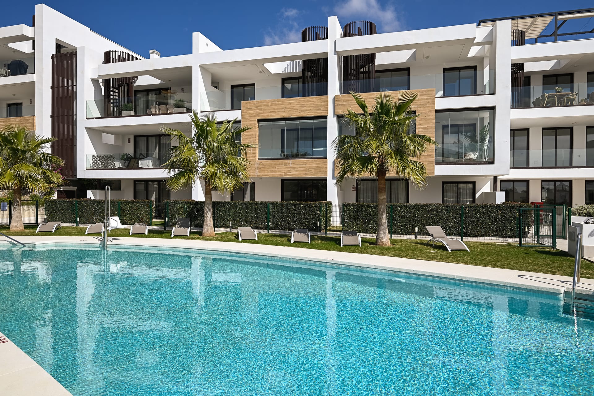 The communal pool along the front of the building, with palms and loungers on the far side. Horizon 36, El Higuerón, Fuengirola.