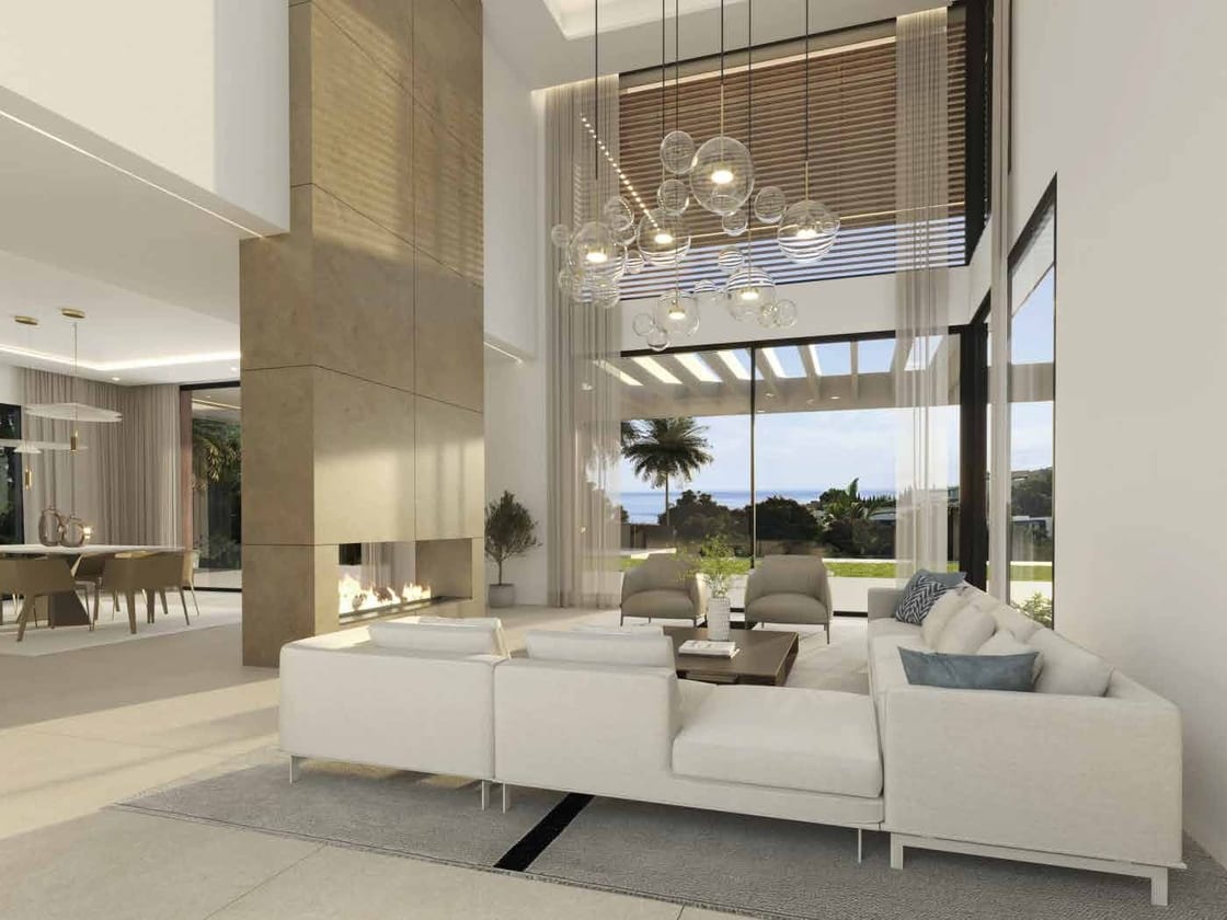 The double-height living room, with a long fireplace set into a tall beige wall and glass doors to the garden. La Alquería Villa, La Alquería, Benahavís.