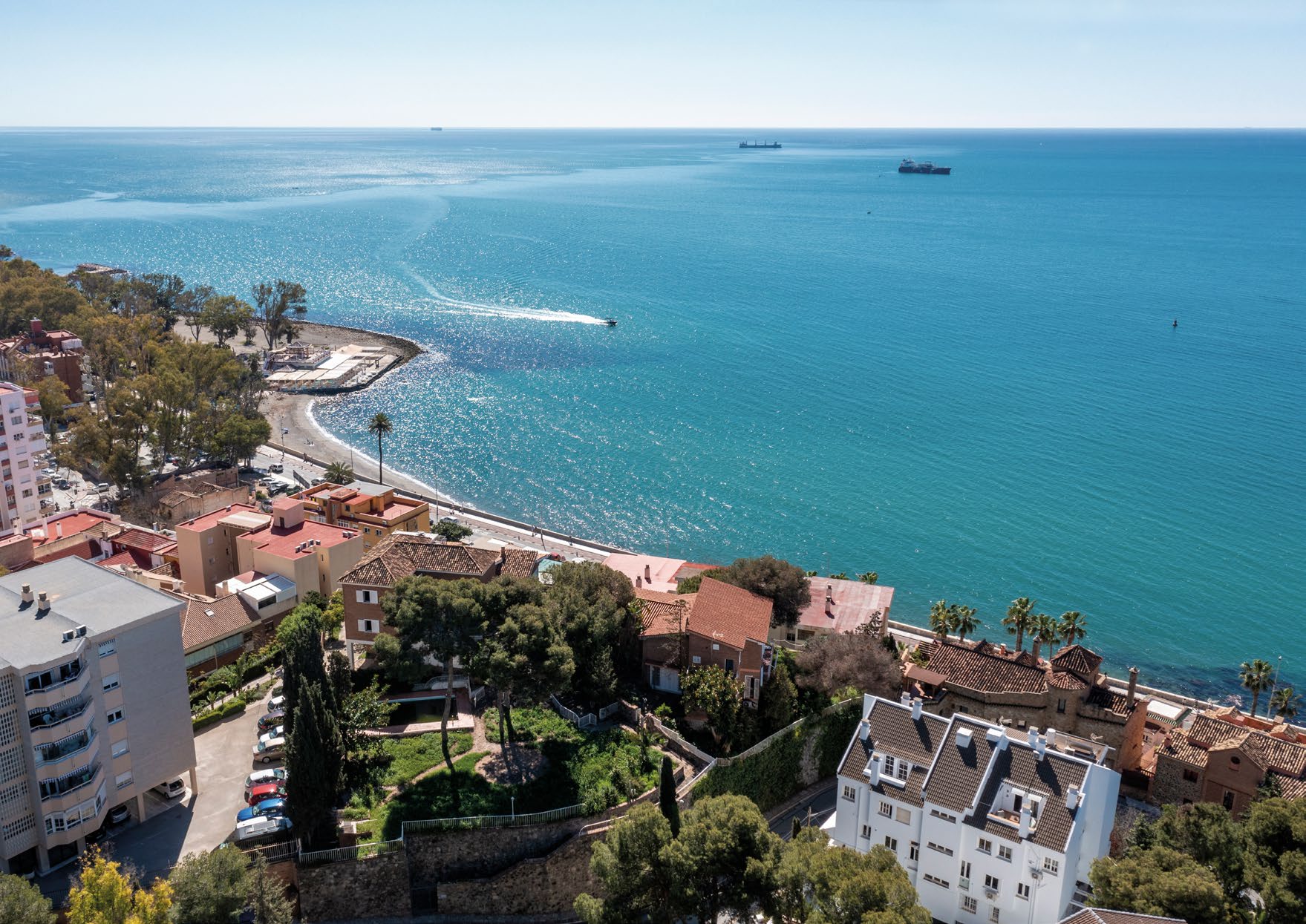 A photograph of the shoreline near the plot, with a curving beach, a small breakwater and the open sea beyond. Livermore, El Morlaco, Málaga.