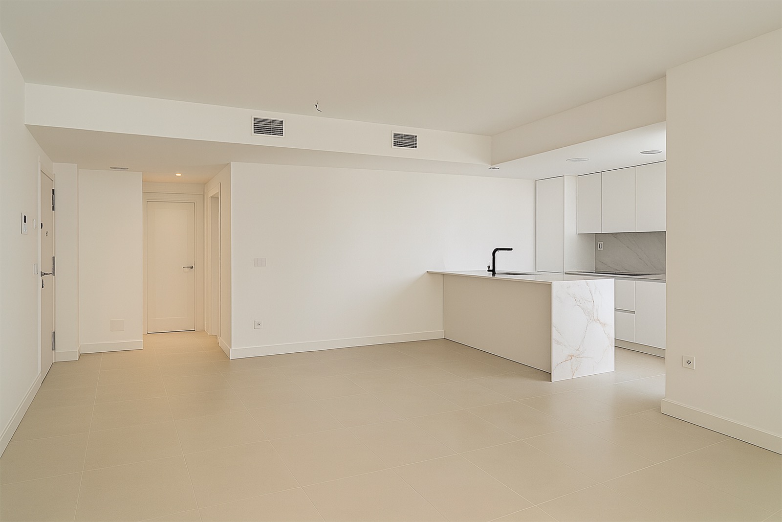 An empty, newly finished apartment at Lomas del Higuerón 2 in Fuengirola: a pale porcelain floor, air-conditioning grilles in the lowered ceiling, bare wires at the light point and a white kitchen with a marble-effect breakfast bar