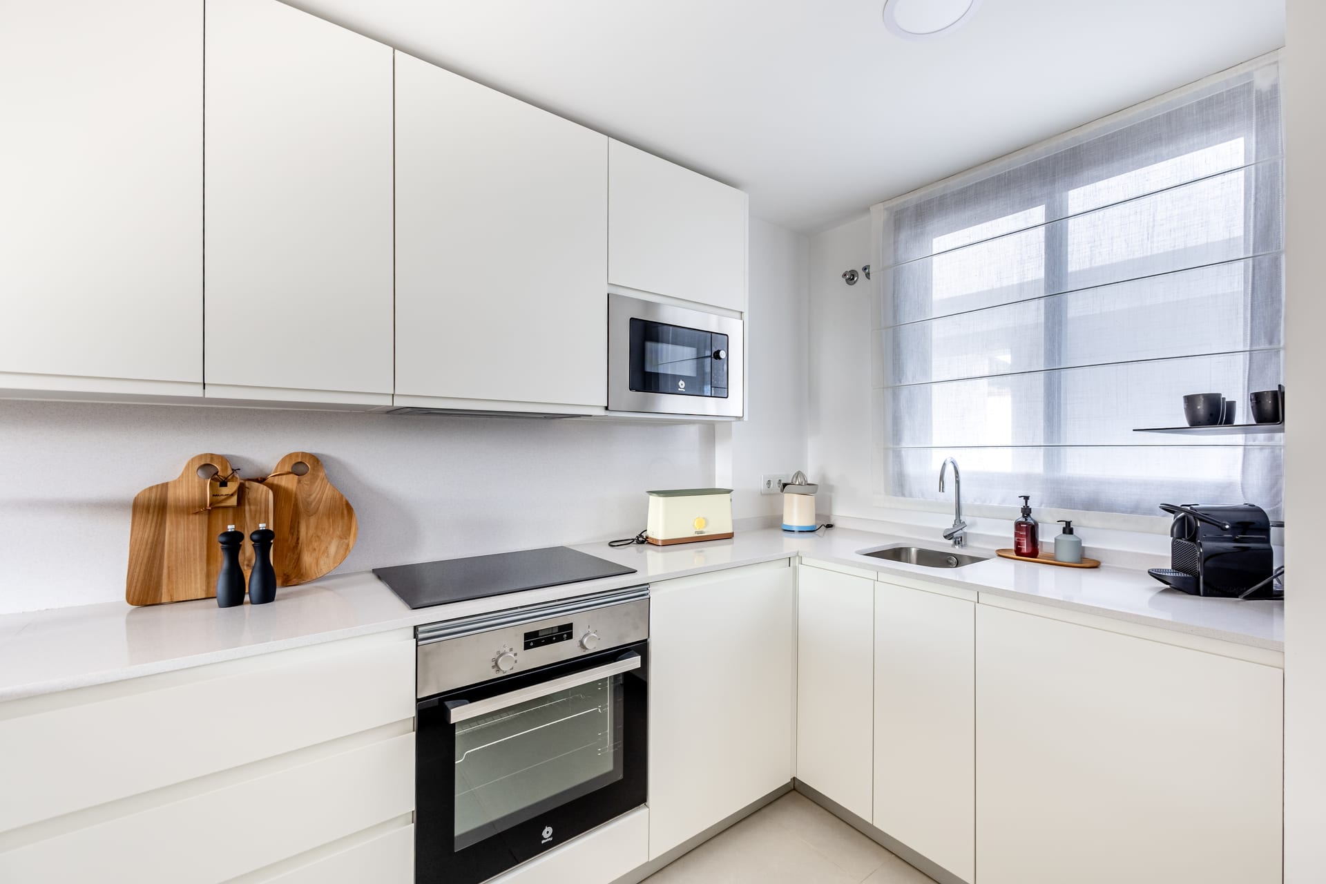 The kitchen of the show penthouse, in white handleless units with the oven, hob and microwave built in and the sink under the window. Lomas del Higuerón 3, El Higuerón, Fuengirola.