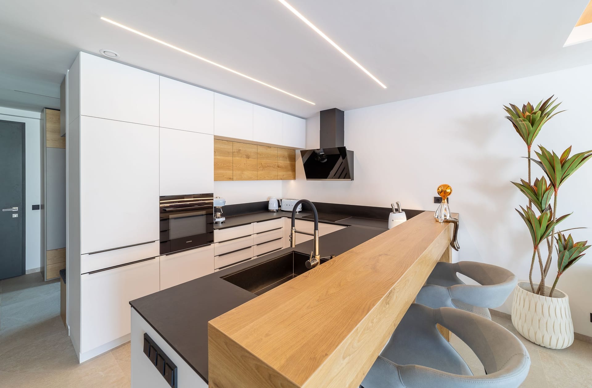The kitchen in one of the villas, with white units, a dark worktop and a wooden breakfast bar. Los Porqueroles, San Pedro de Alcántara, Marbella.