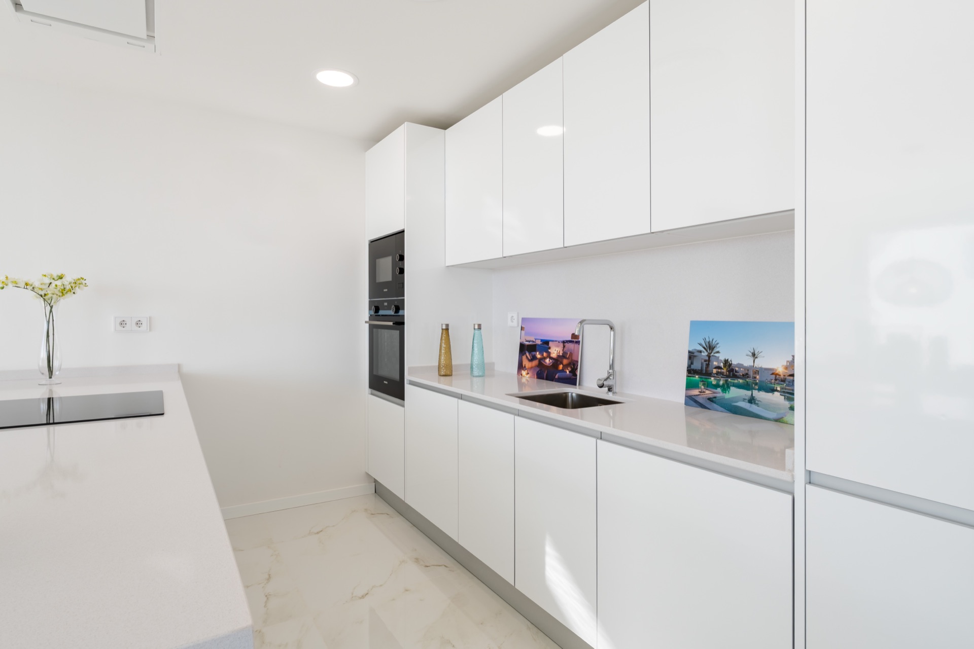 The kitchen in a show home, with white gloss units and a white quartz worktop. Mãla Kai Resort, Valle Romano, Estepona.