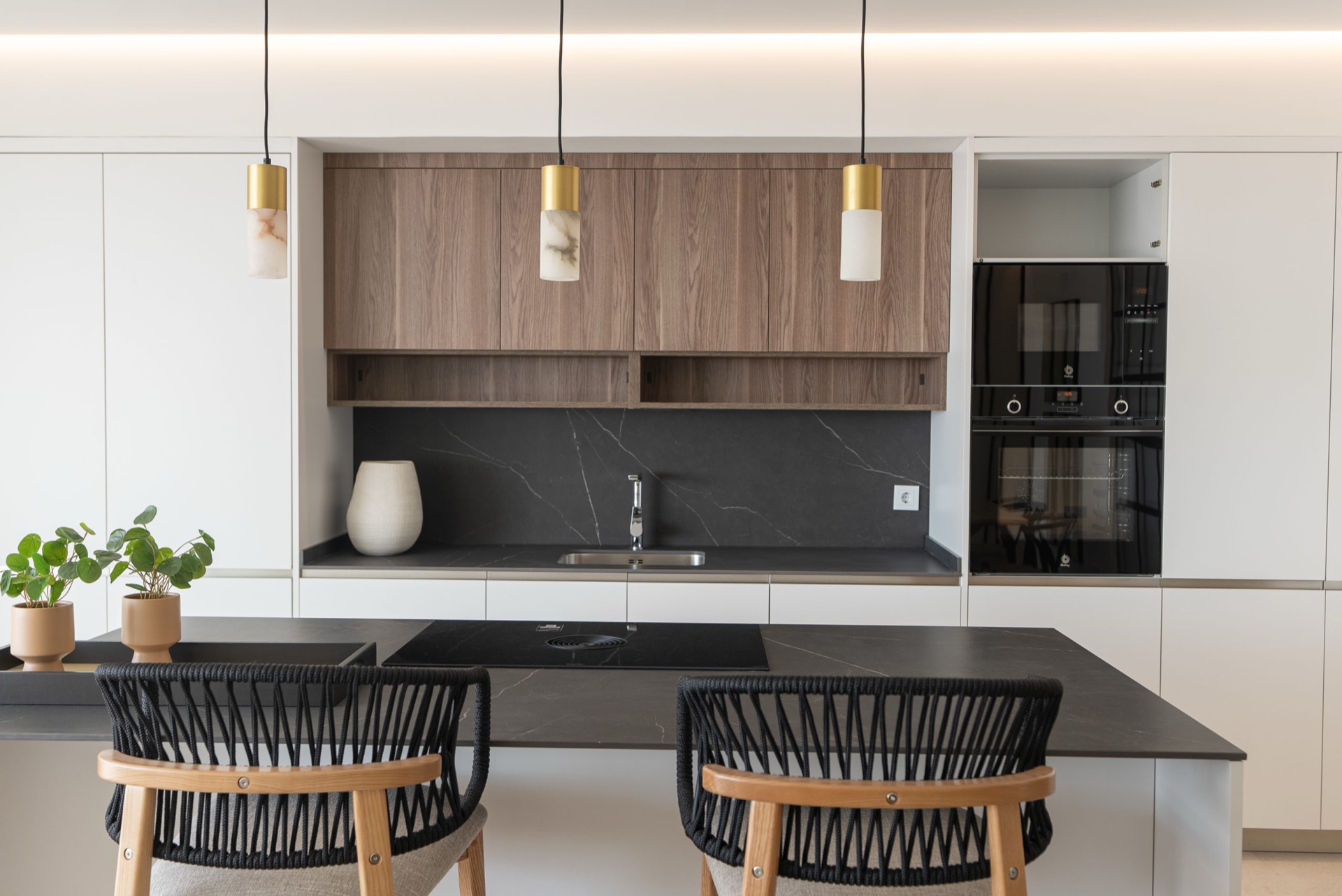 The kitchen of a finished home in the first stage, with white units, wood-grain wall cupboards, a dark marble-effect worktop and an induction hob set into the island. Mirador de Estepona Hills, Altos de Estepona, Estepona.