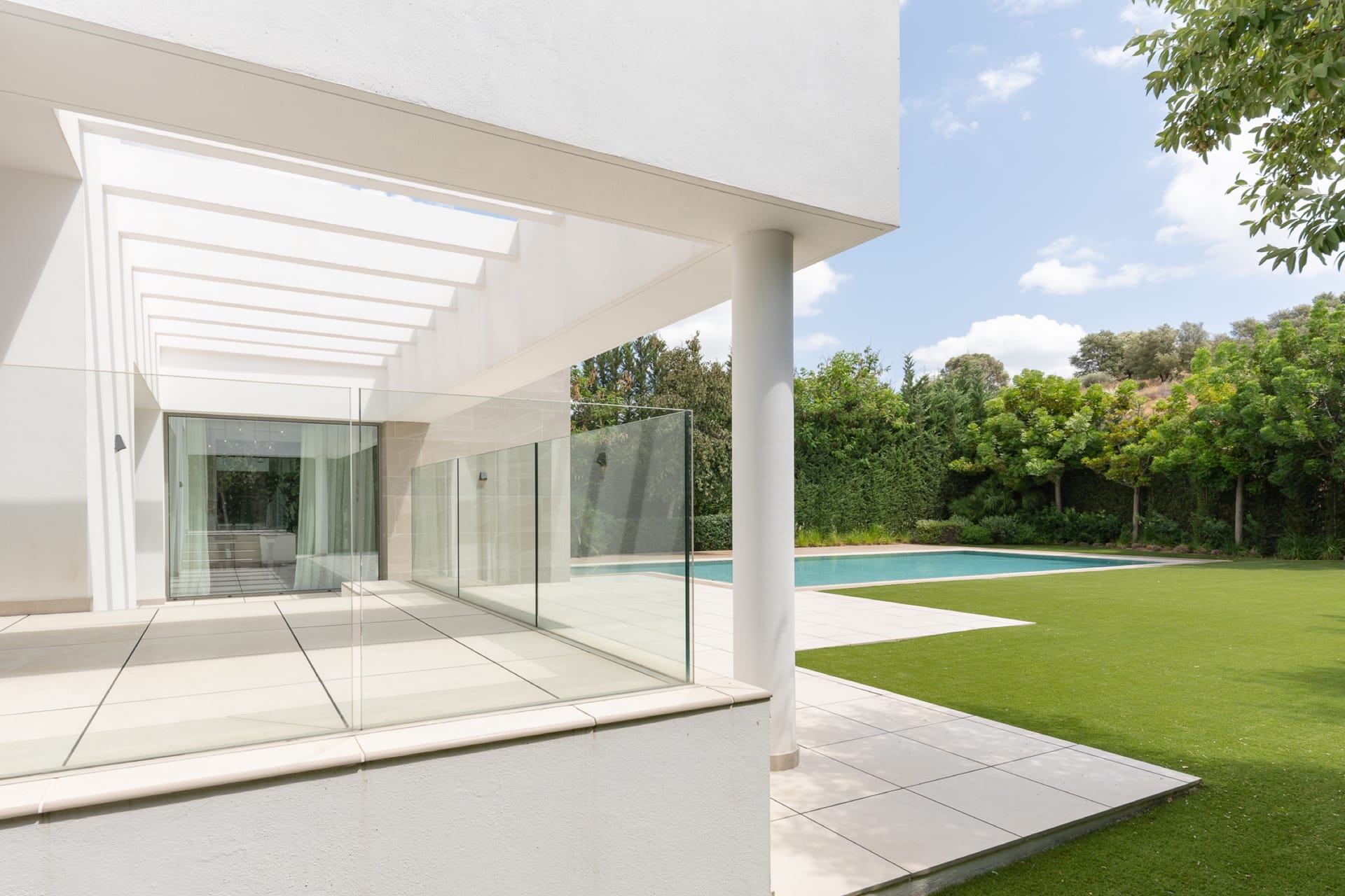 A covered terrace beside the lawn, with the pool beyond. Nine in Paradise, El Paraíso, Estepona.