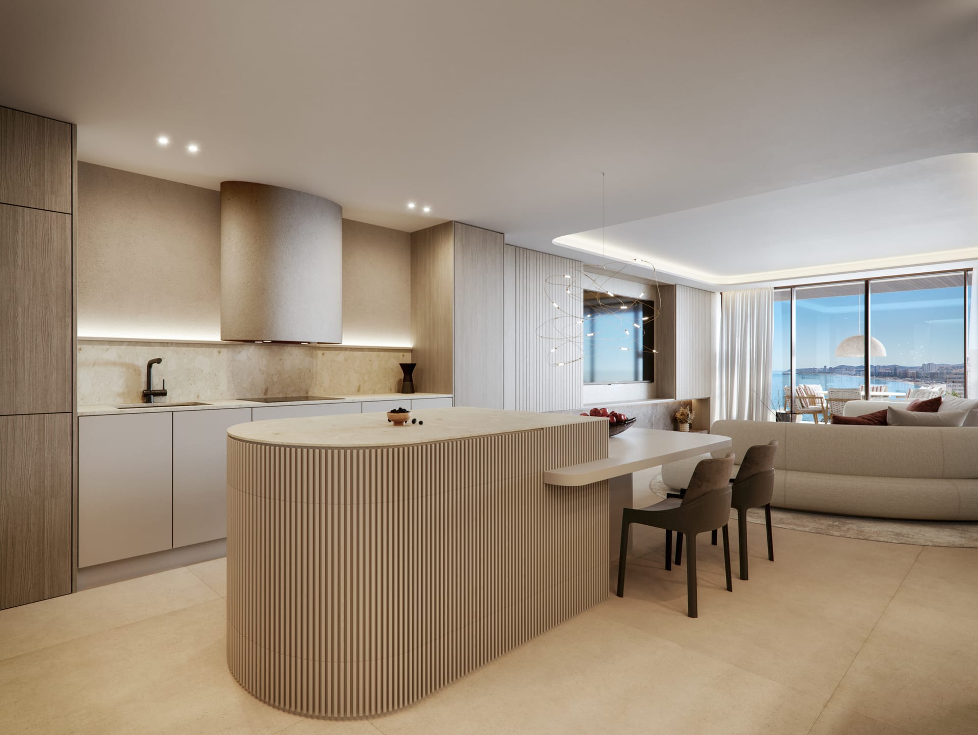 The kitchen, with pale units and a rounded, ribbed island with a breakfast bar, open to the living room and its terrace. Óleo, Carvajal, Fuengirola.