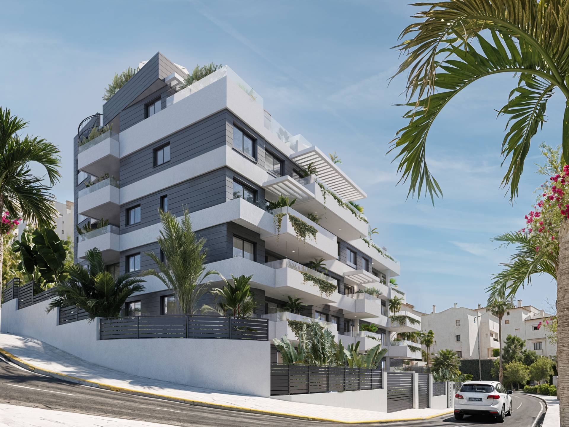 The building on its street corner, behind a slatted metal fence and planted beds, with white apartment buildings further down the road. Portamare, Puerto de Estepona, Estepona.