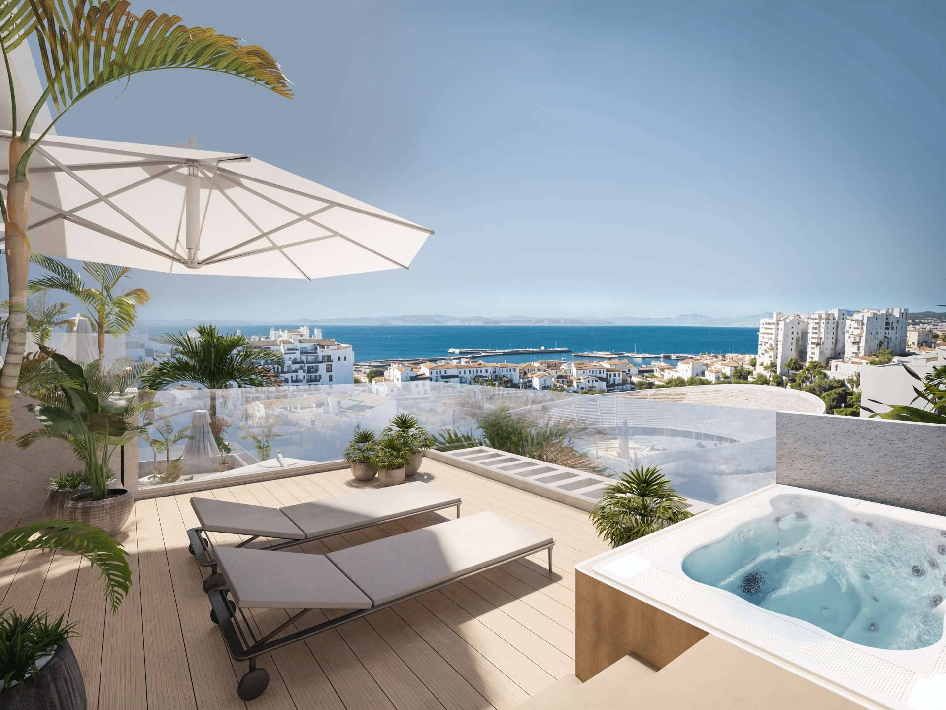 A penthouse roof terrace with sun loungers, a parasol and a private jacuzzi, looking over the white buildings of Estepona to the marina and the sea. Portamare, Puerto de Estepona, Estepona.