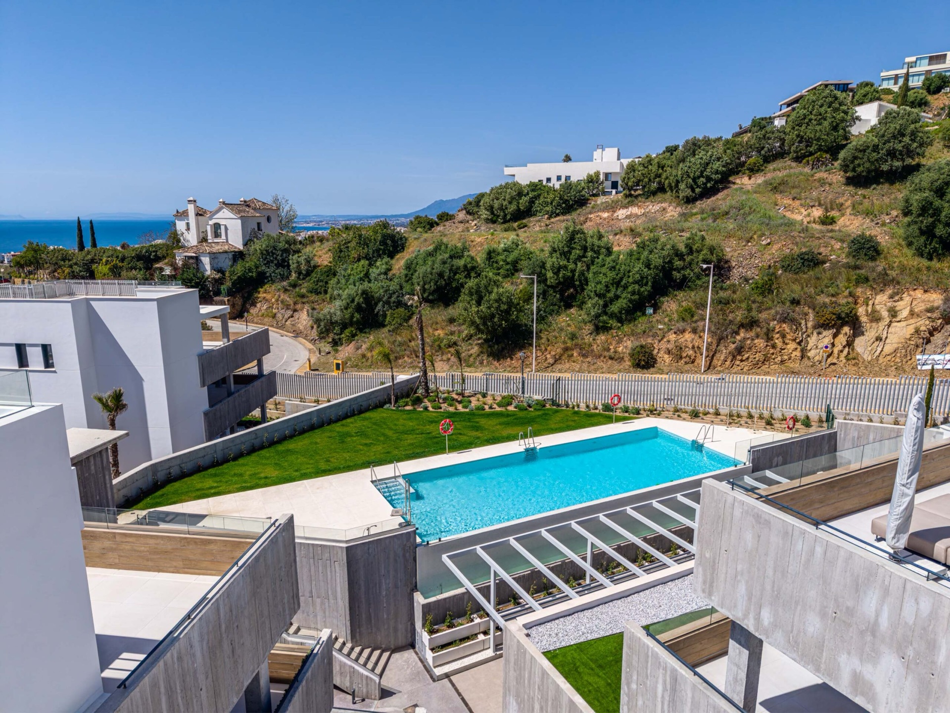 The outdoor pool on its lawn, with the sea visible over the hillside beyond the fence. Quintessence, Altos de los Monteros, Marbella.