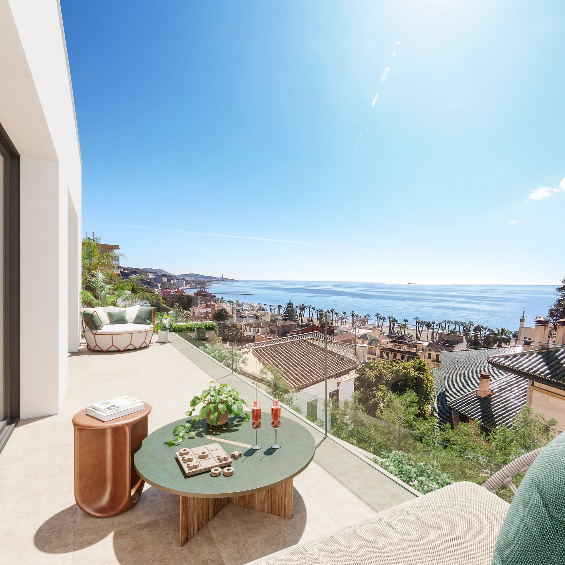 A terrace with a glass balustrade, a round table and a lounge chair, looking over tiled roofs to the beach and the coast. Ramal de Monte Sancha, Monte Sancha, Málaga.