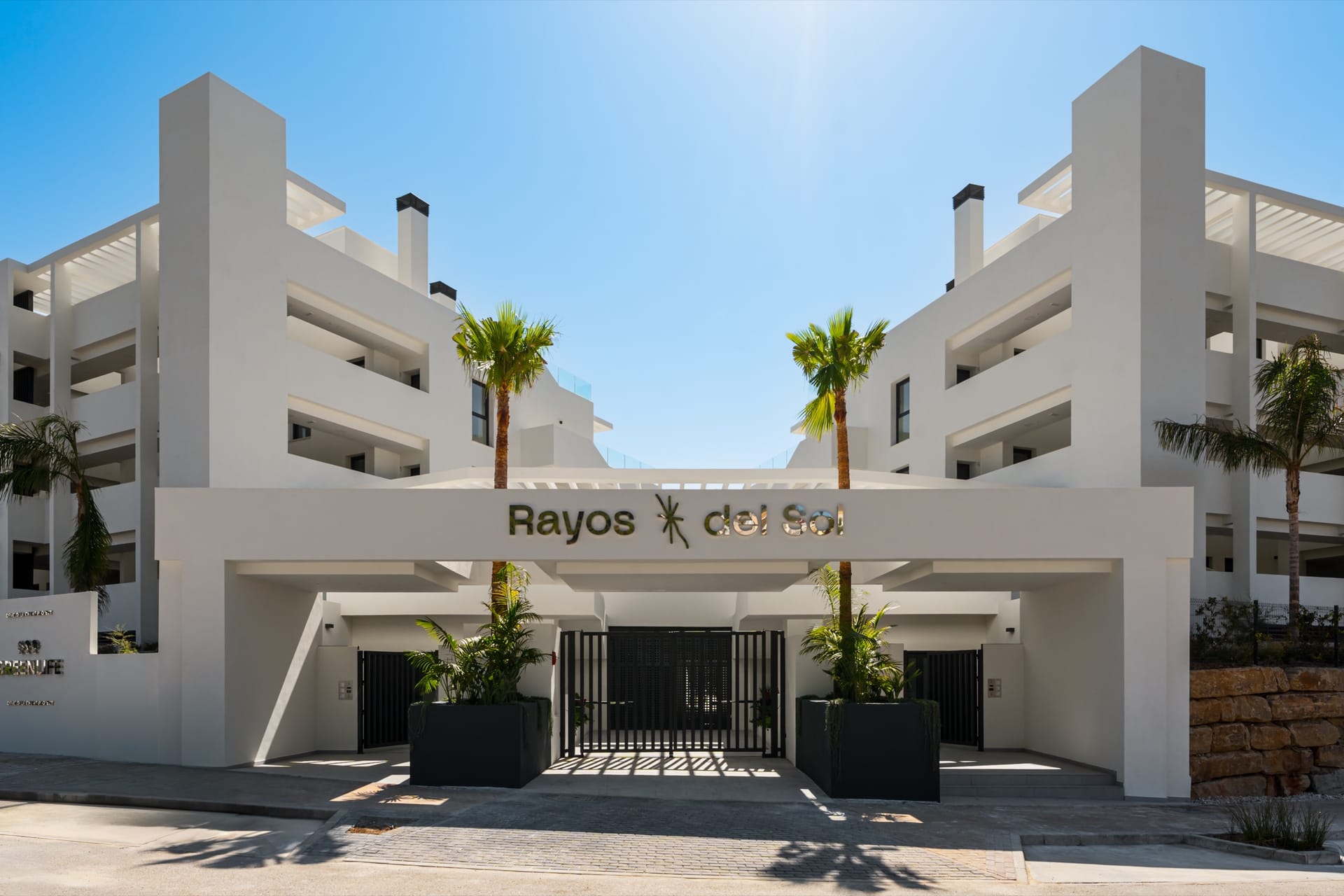 The gated entrance, with the name of the building above it and a palm on either side. Rayos del Sol, El Chaparral, Mijas.