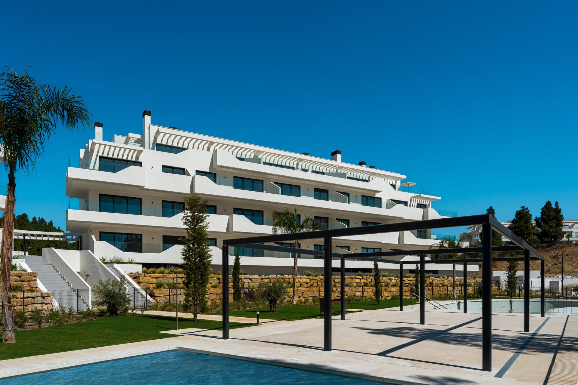 A black steel pergola beside the pool, with the buildings rising behind it. Rayos del Sol, El Chaparral, Mijas.