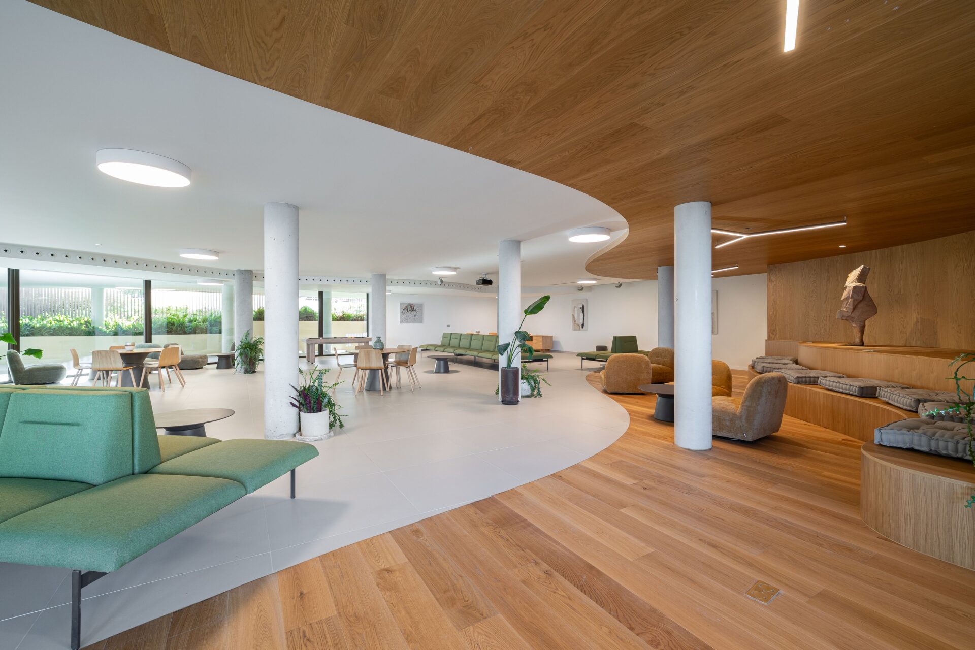 A shared lounge indoors, with sofas, a wood-lined ceiling and a wall of glass onto the gardens. South Residences, El Higuerón, Fuengirola.