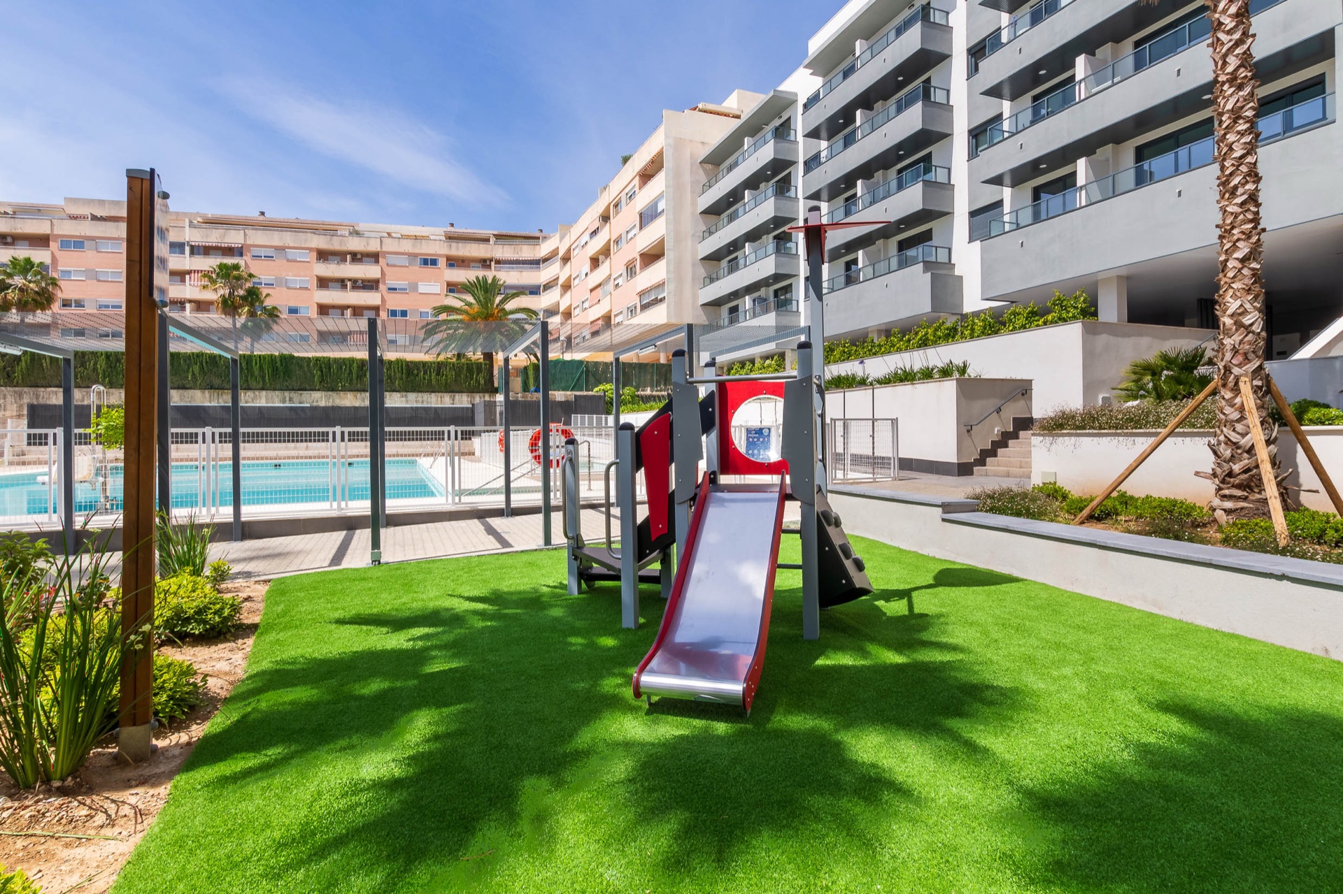 The children’s playground on the lawn, with the buildings behind it and the pool beyond the fence. Suite Mijas Phase One, Las Lagunas de Mijas, Mijas.