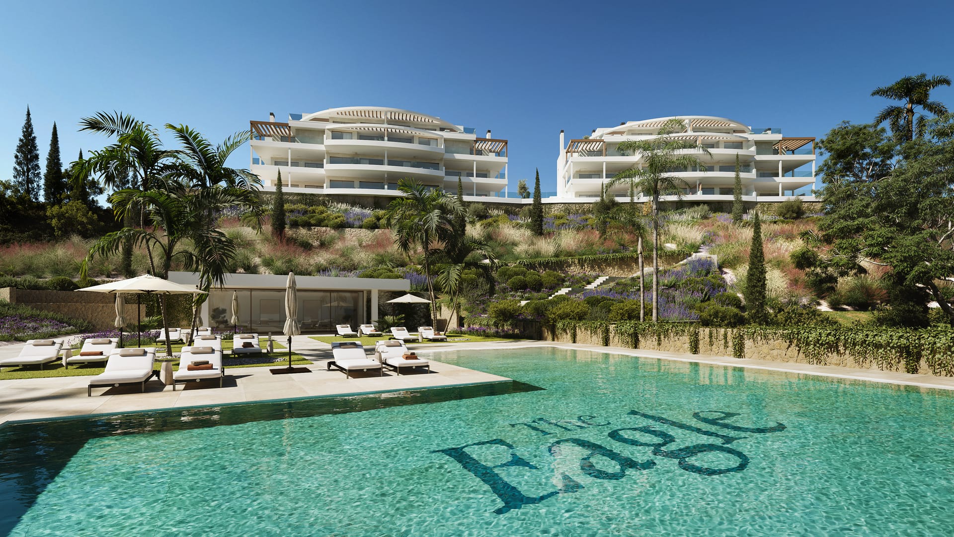 The pool below the buildings, with sun loungers on its deck and a glass-fronted pavilion at the foot of the planted slope. The Eagle Residences, Hipódromo, Mijas.