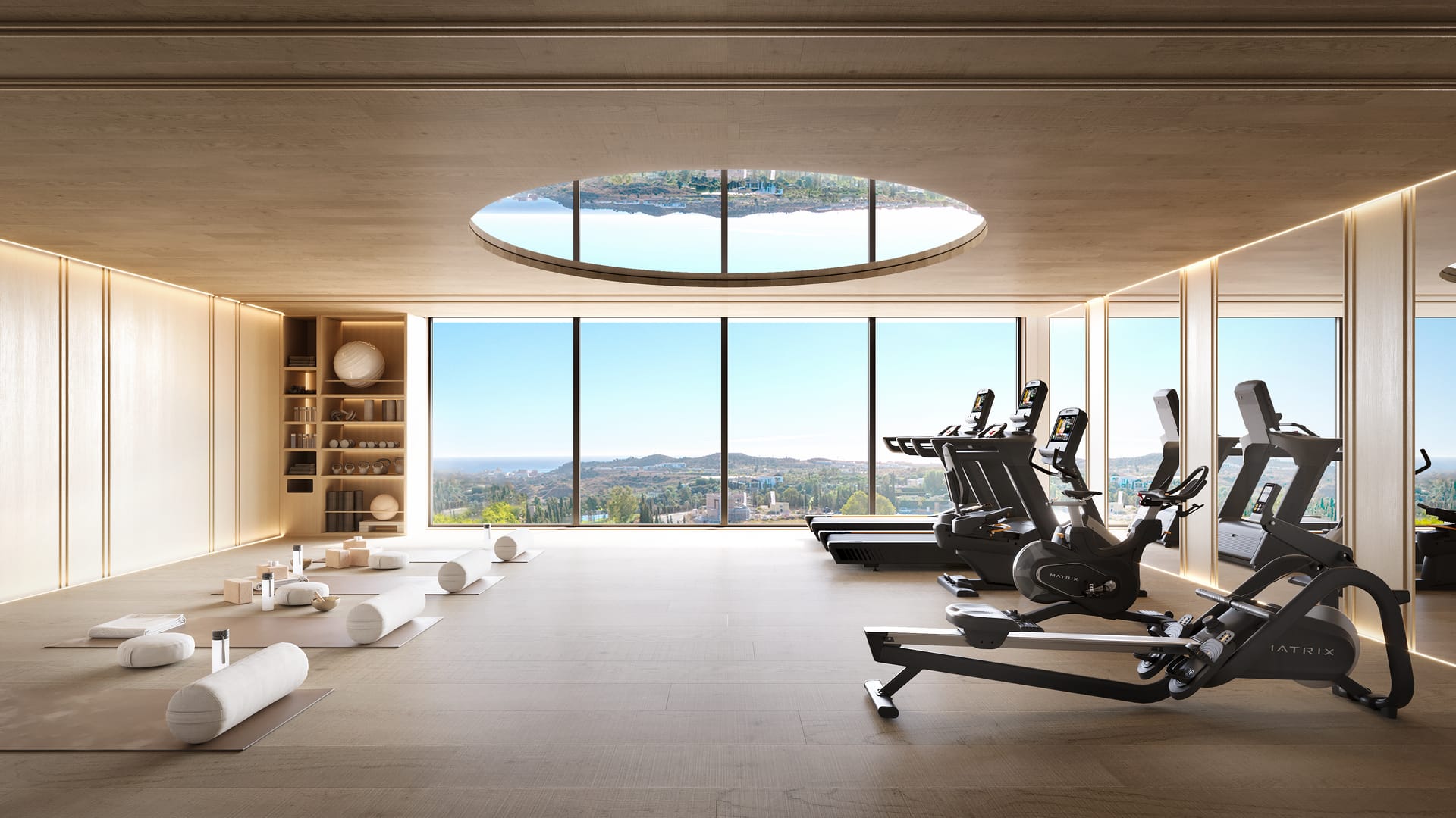 The gym, with running machines and a rowing machine beside a wall of glass, exercise mats on the floor and a round skylight in the ceiling. The Eagle Residences, Hipódromo, Mijas.