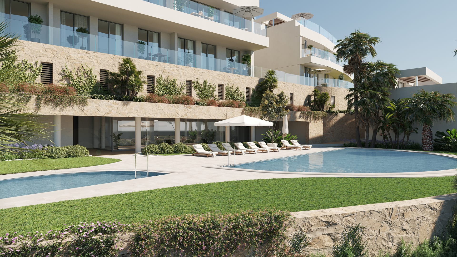 The shared pools at the foot of the scheme, with sun loungers on the lawn beside them. The Kos, El Higuerón, Fuengirola.