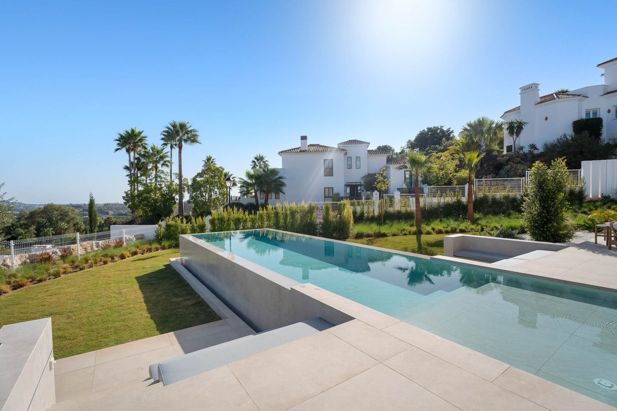 The long infinity pool in the garden of the finished villa, with the hillside and the neighbouring houses behind. Tree Villas, La Cala Golf, Mijas.