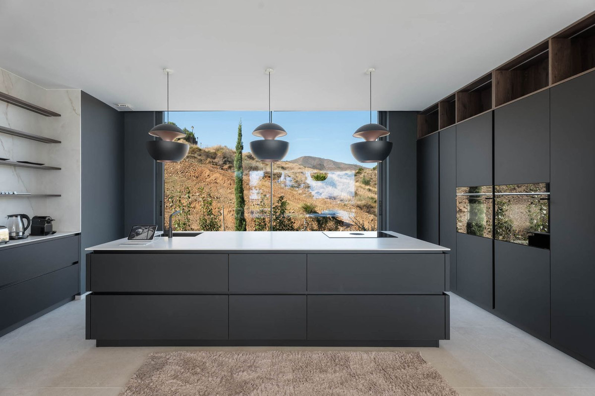 The kitchen in the finished villa, with a black island under three pendant lights and a window onto the hillside. Tree Villas, La Cala Golf, Mijas.