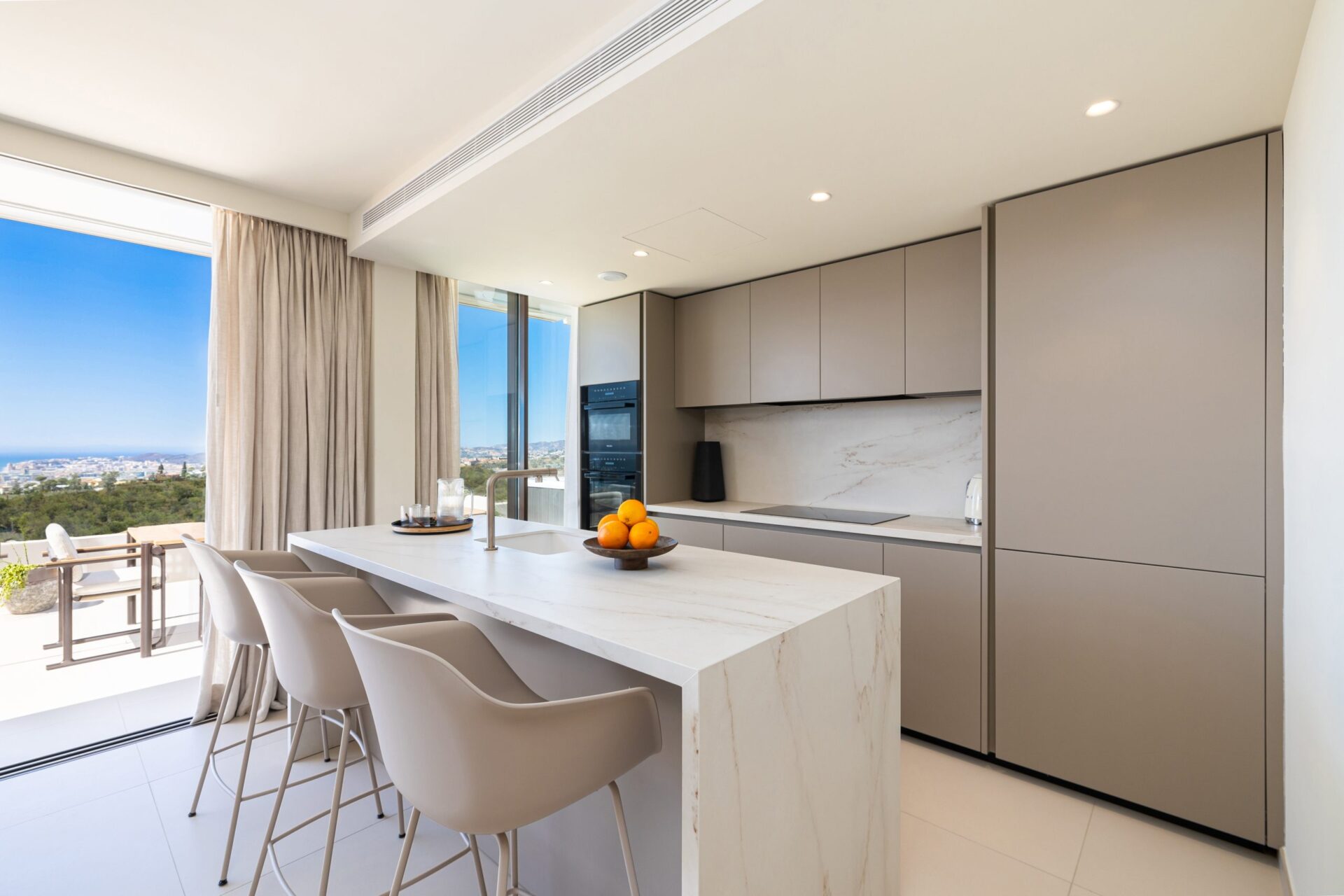 The kitchen, with a white stone island and the coast beyond the terrace. Valley Collection, El Higuerón, Fuengirola.