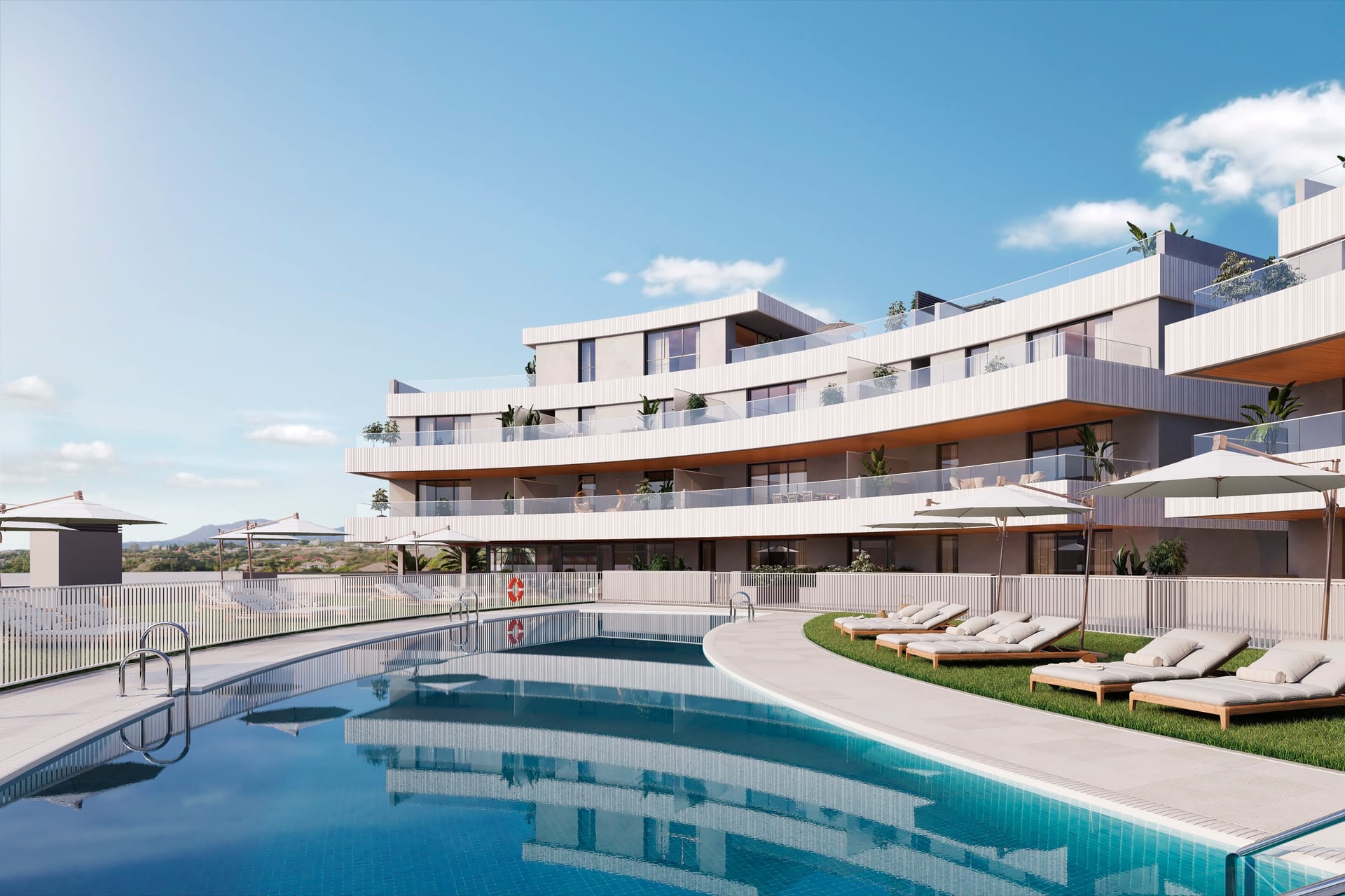 The pool beside a lawn with sun loungers, below the curved terraces of the buildings. Vanian Views, La Resina, Estepona.