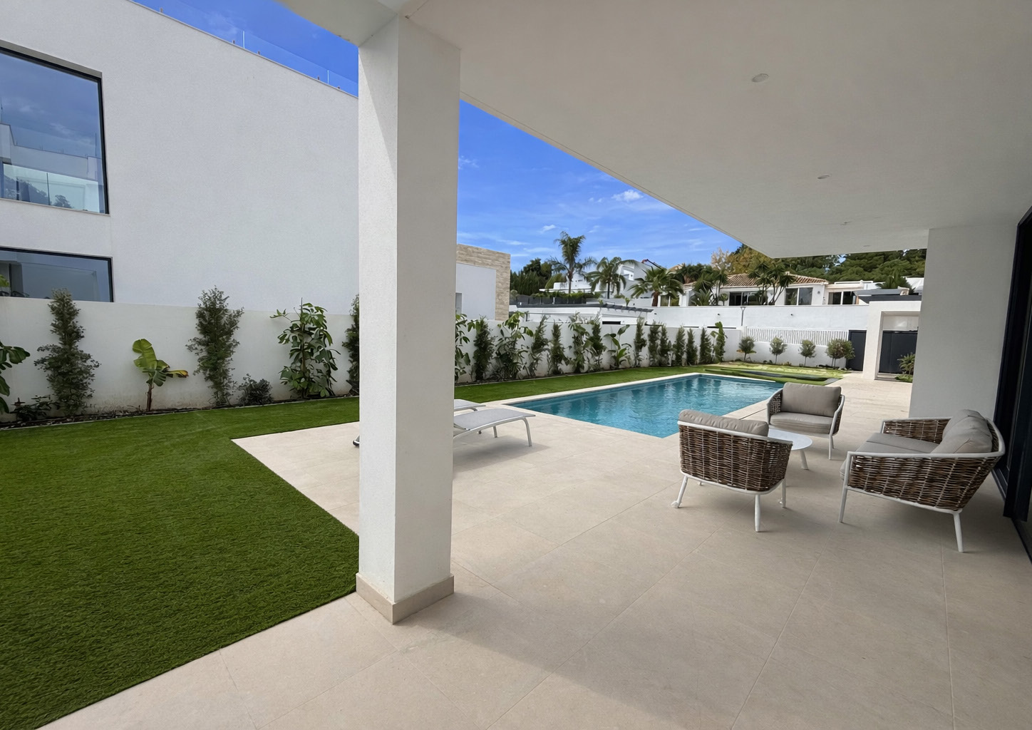 A covered terrace with outdoor seating, looking across the lawn to the pool. Villa Dunas, Nueva Atalaya, Estepona.