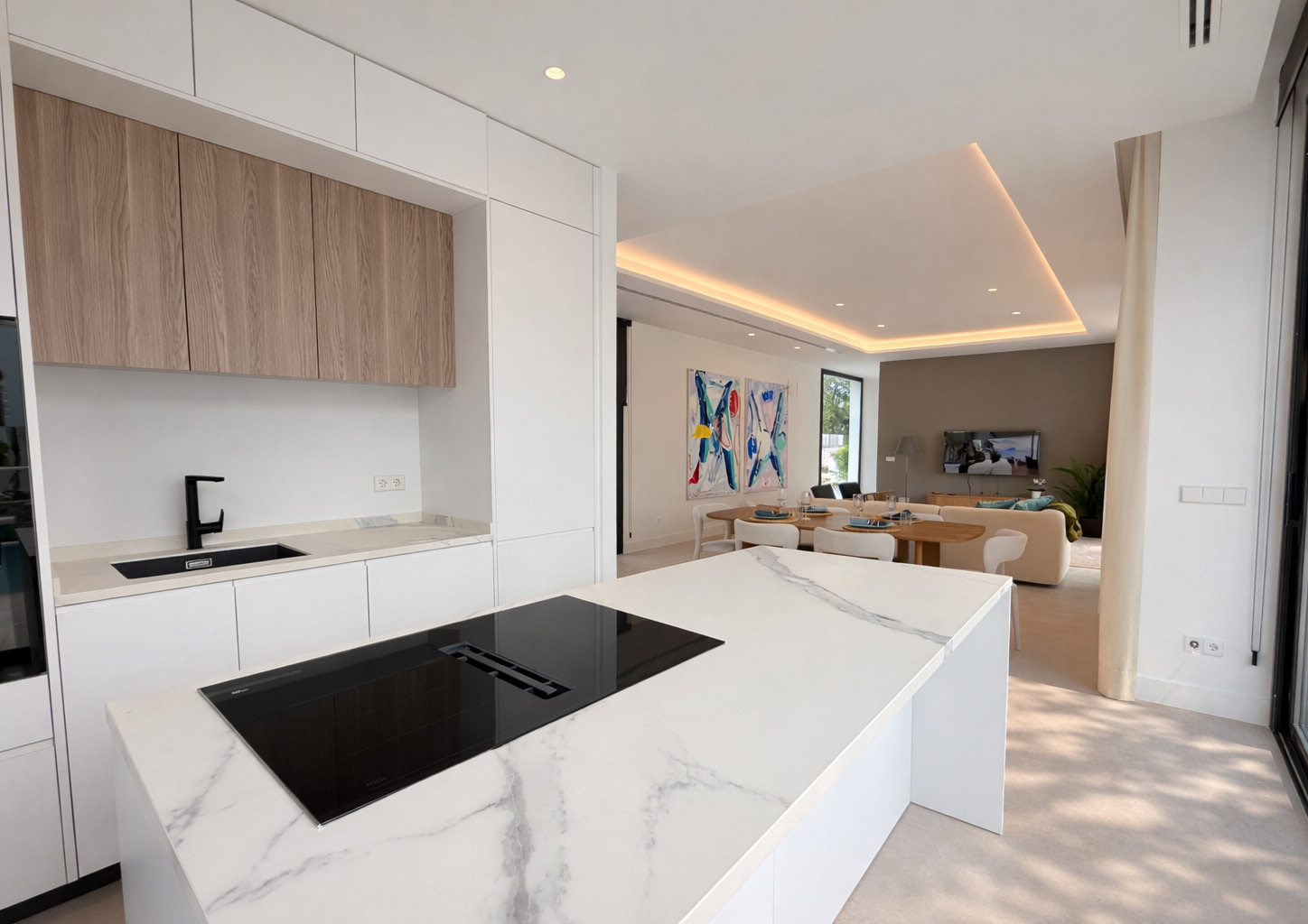 The kitchen, with an island in white veined stone holding the induction hob, and the living room beyond. Villa Dunas, Nueva Atalaya, Estepona.